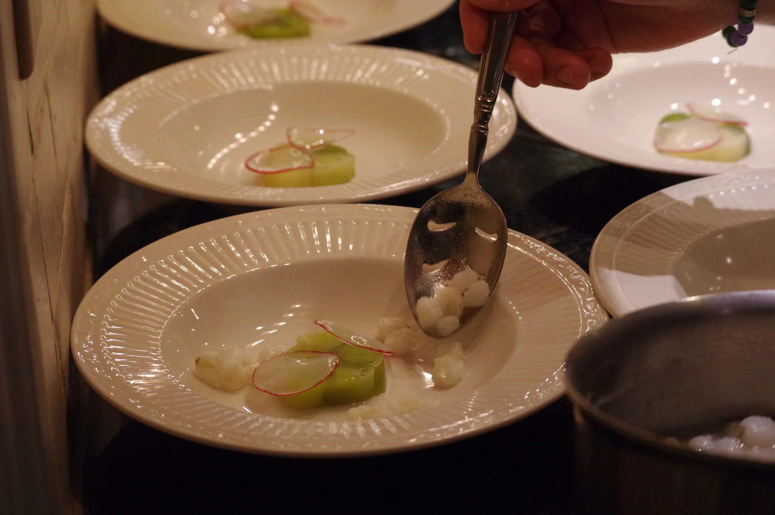 Plates with sliced radishes, celery, and cheese, with a person serving food with a spoon.
