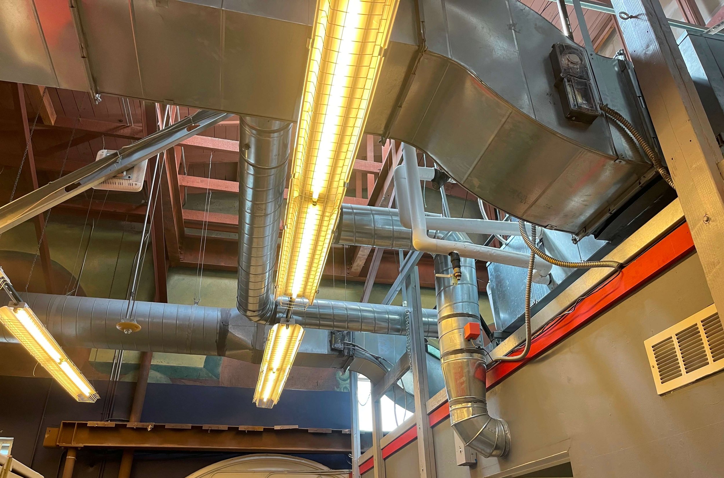 Ceiling with industrial air ducts, bright yellow fluorescent lights, and a vent.