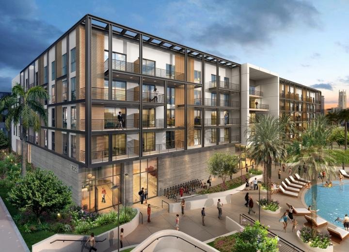 Modern multi-story apartment building with large balconies and glass walls, surrounded by palm trees and landscaping, with outdoor pool and people walking around.