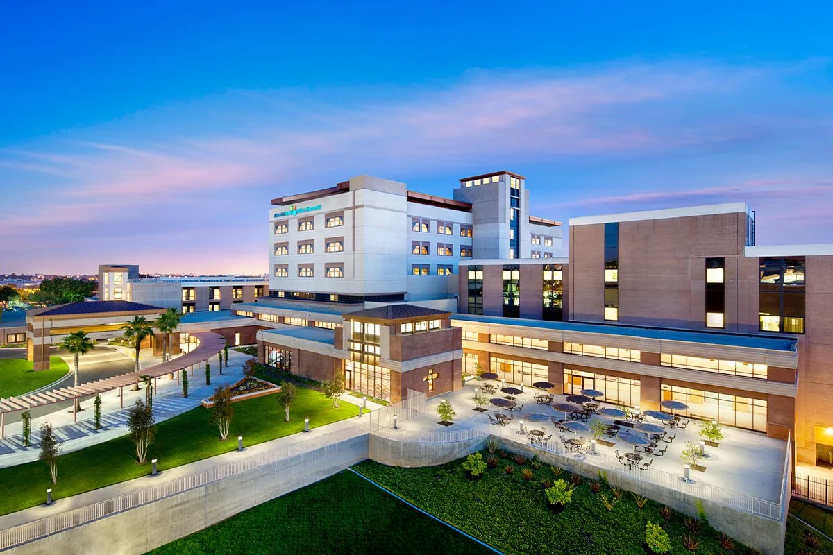 Modern hospital building with outdoor seating area and landscaped surroundings at dusk.
