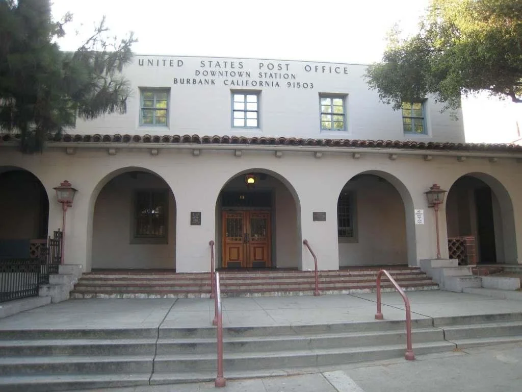 Front view of the United States Post Office building in Burbank, California, with arched entryway, steps, and trees.