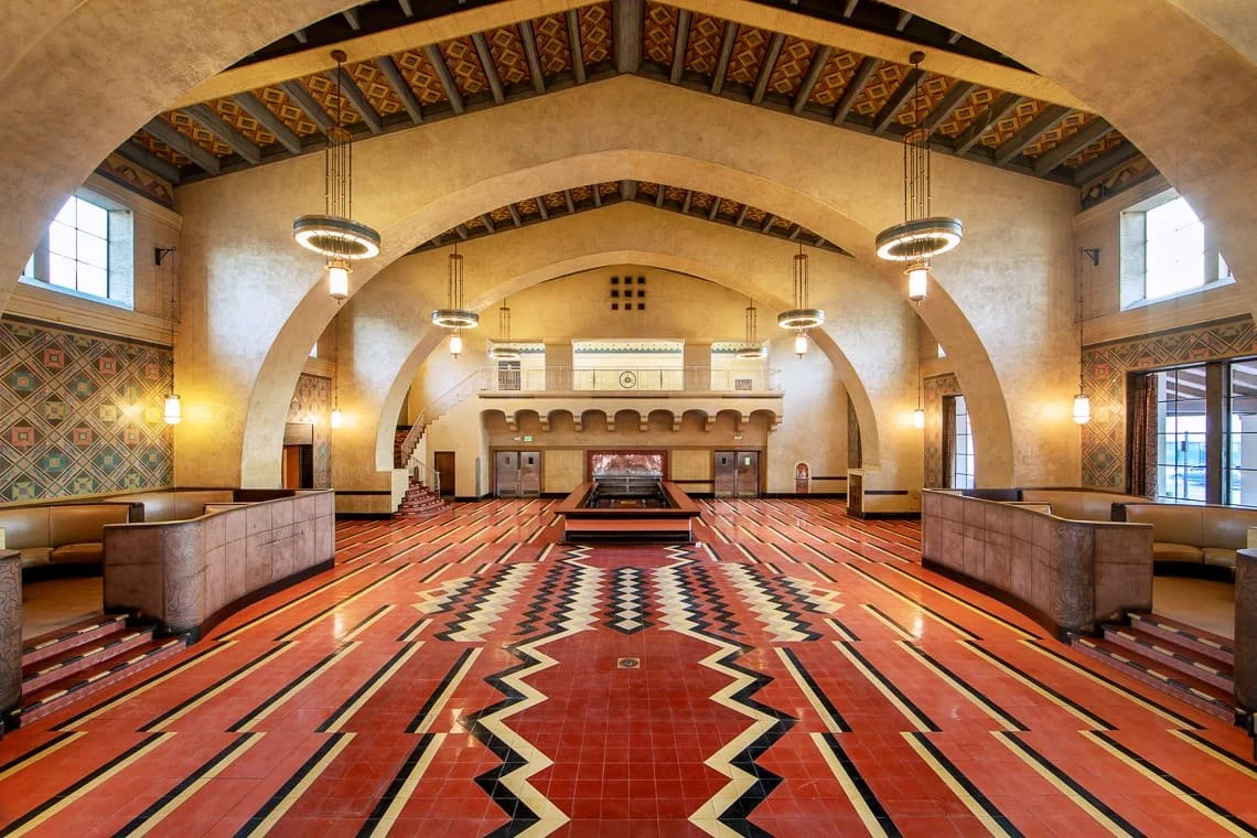 An elegant, spacious lounge with high vaulted ceilings, arched beams, decorative lighting, and a colorful geometric tile floor.