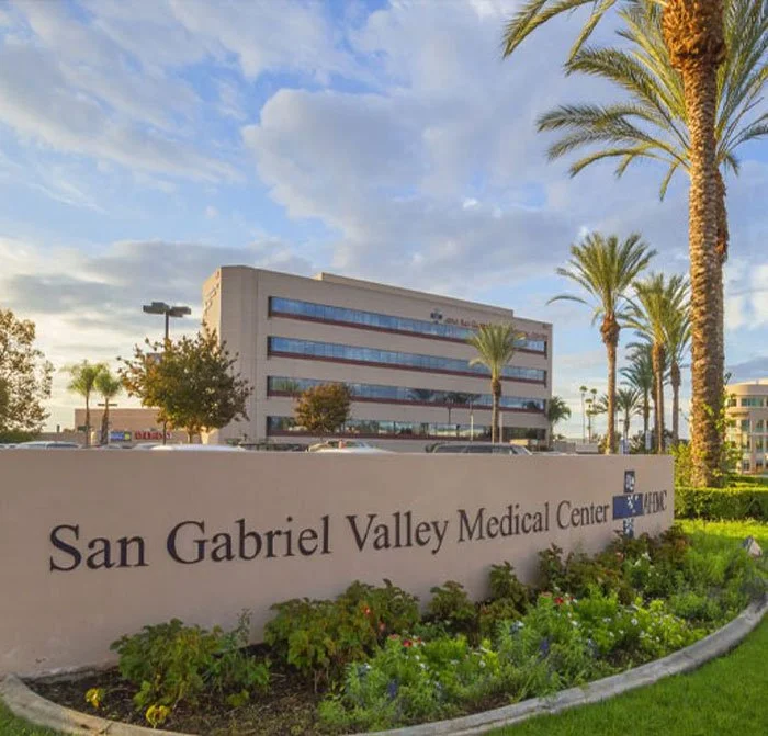 Exterior view of San Gabriel Valley Medical Center with a large sign, palm trees, and a multi-story office building in the background on a sunny day.
