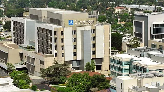 Aerial view of the City of Hope medical center building in a cityscape with other buildings and greenery.