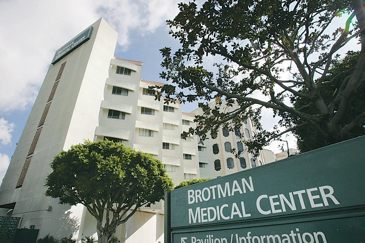 Low-angle view of the Brotman Medical Center building with a sign in the foreground, showing trees and a partly cloudy sky.
