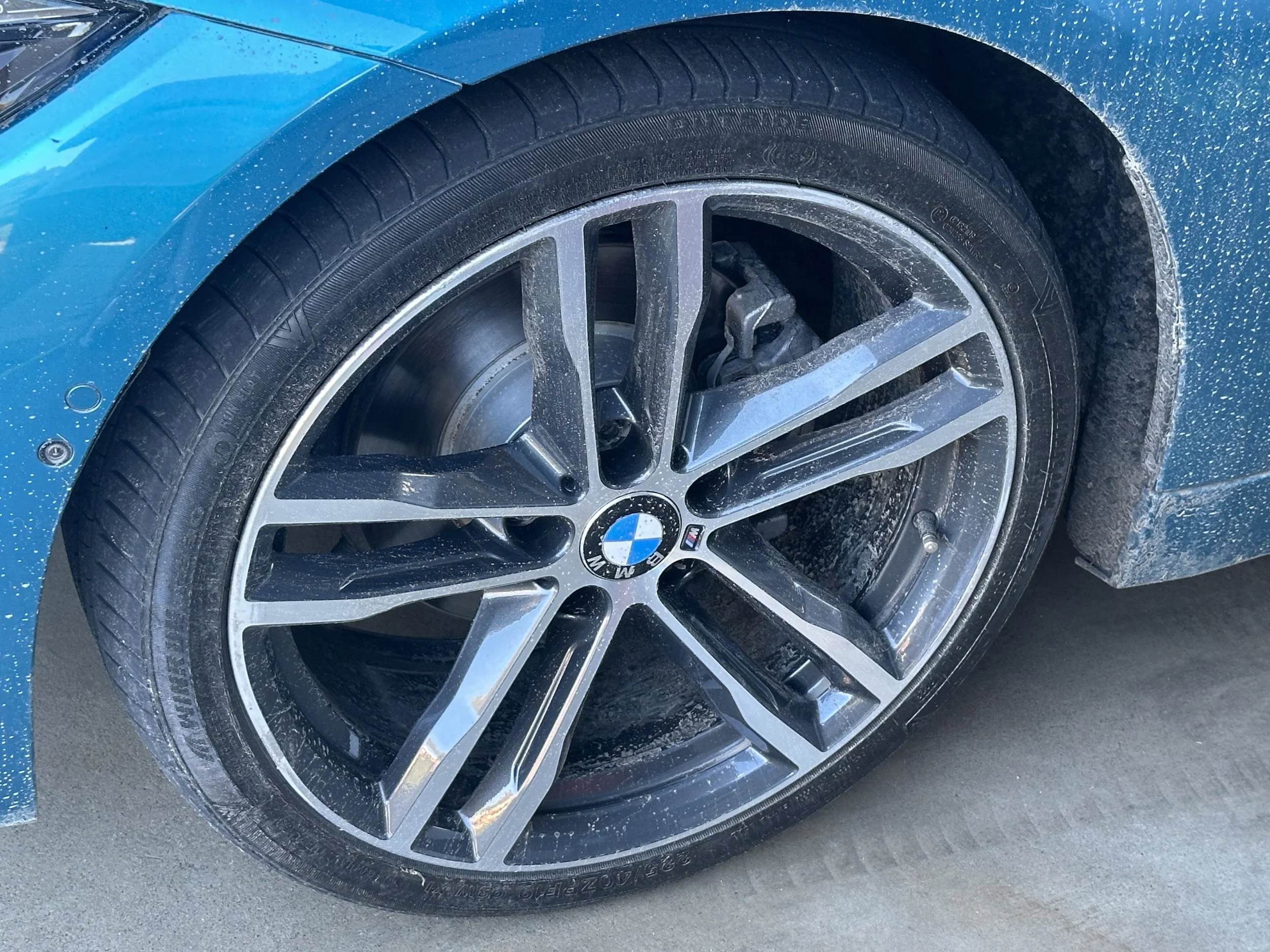 Close-up of a blue BMW car wheel and tire, with a wet and slightly muddy ground.