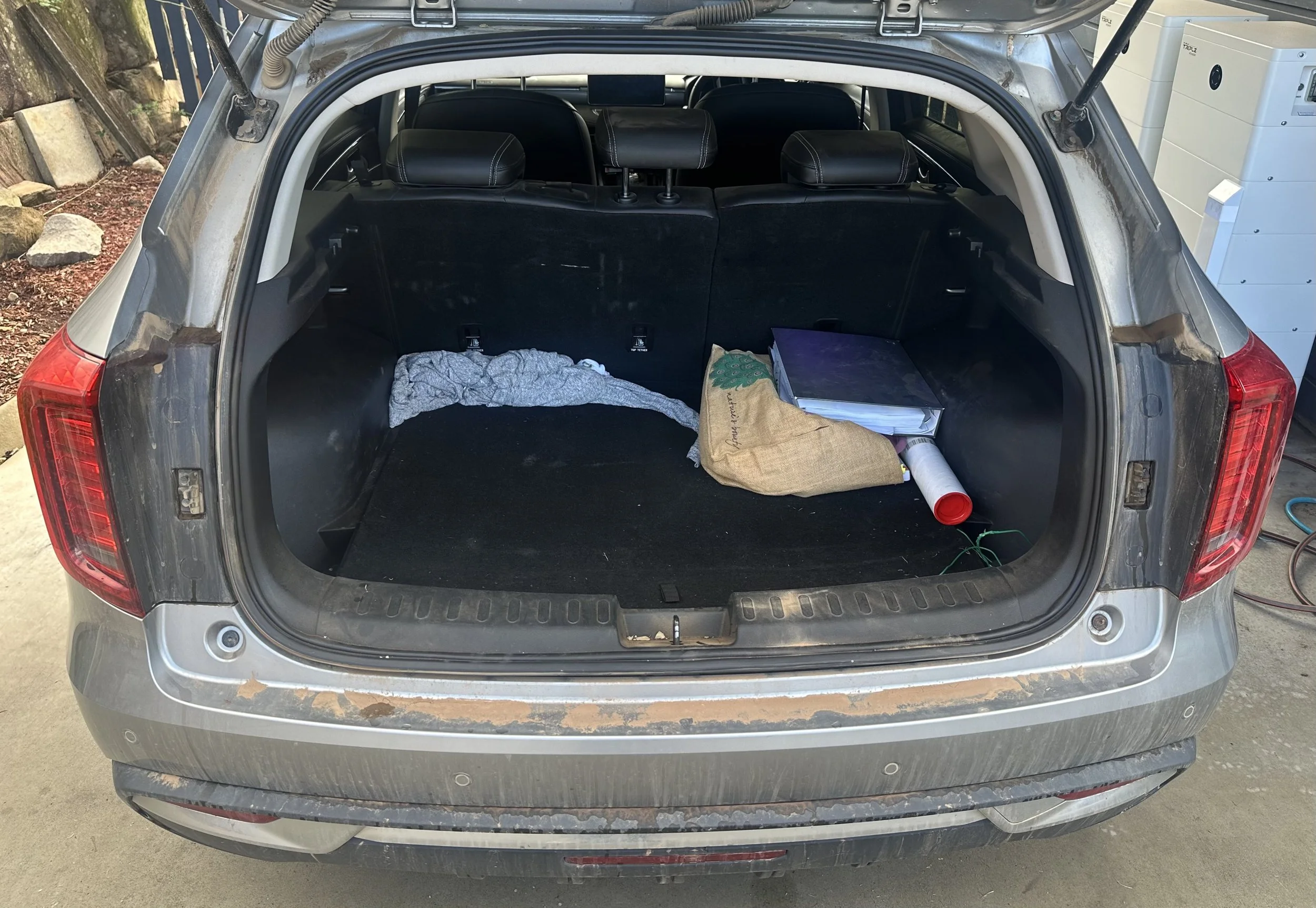 Rear view of an SUV with the trunk open, showing the interior and items stored inside, including a piece of cloth, a brown paper bag, and a white pipe.