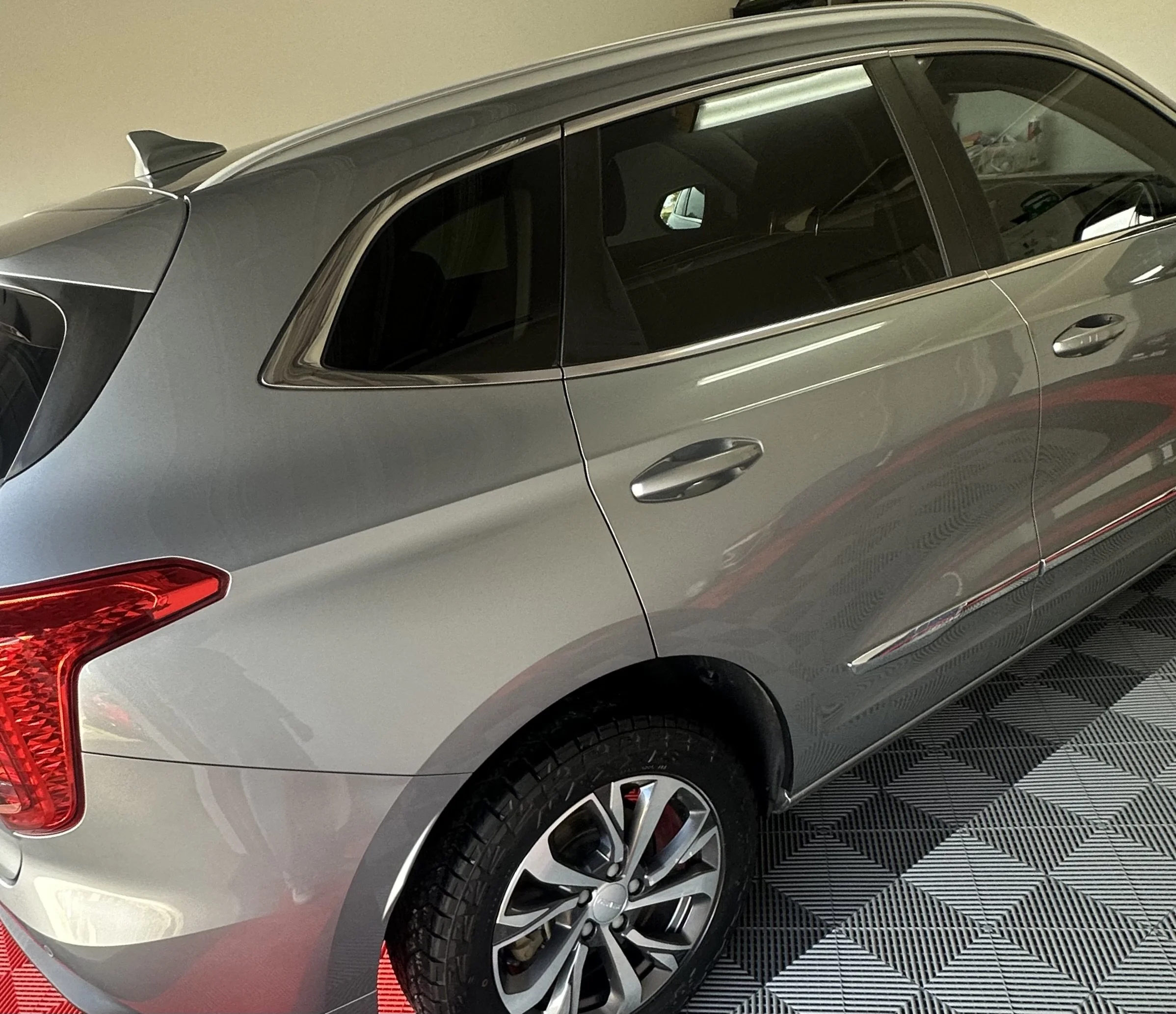 Close-up side view of a gray modern SUV parked indoors, showing the rear side window, wheel, and part of the rear light.