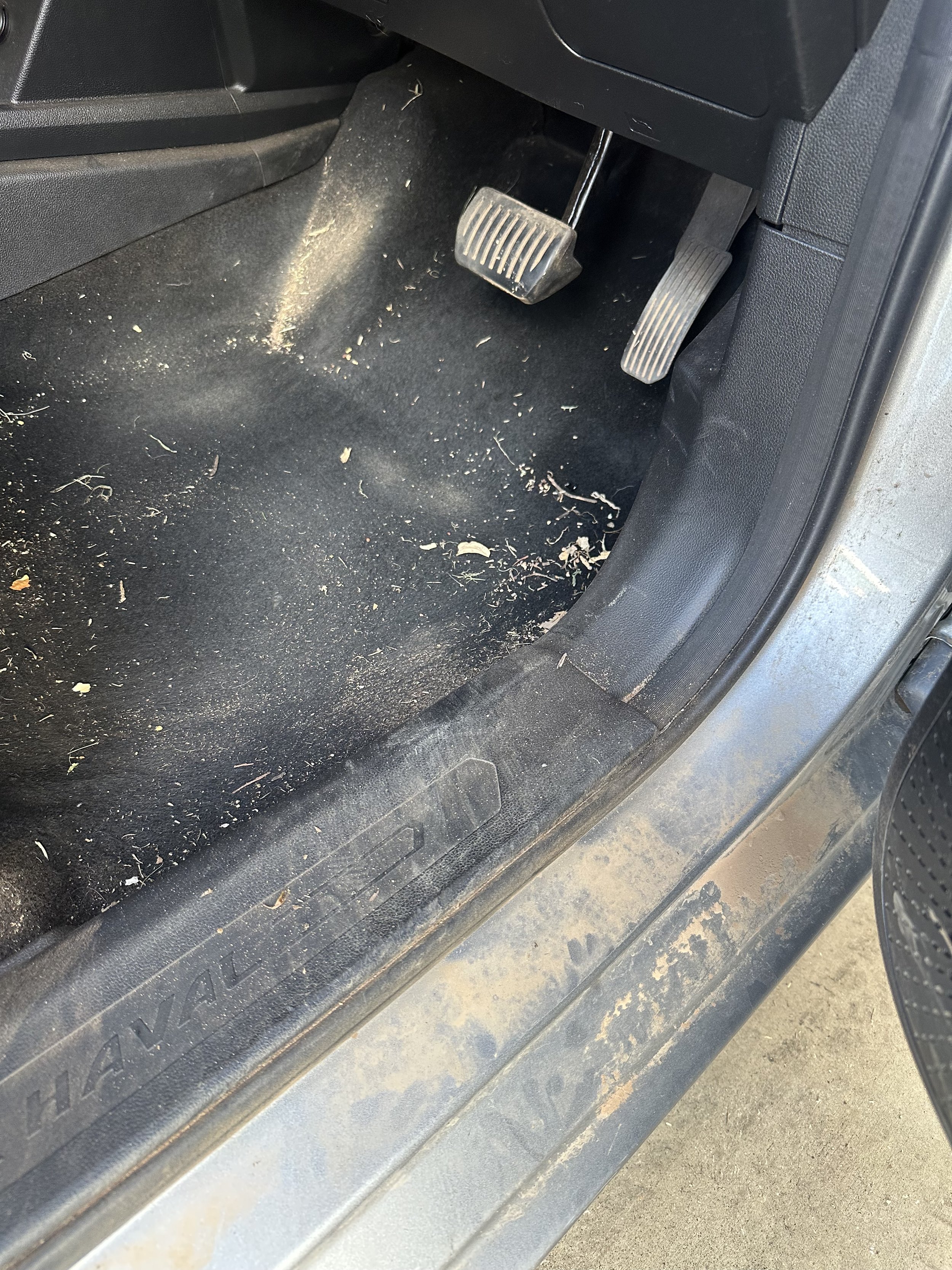 Car interior floor with dirt, debris, and two pedals, accelerator and brake, visible.