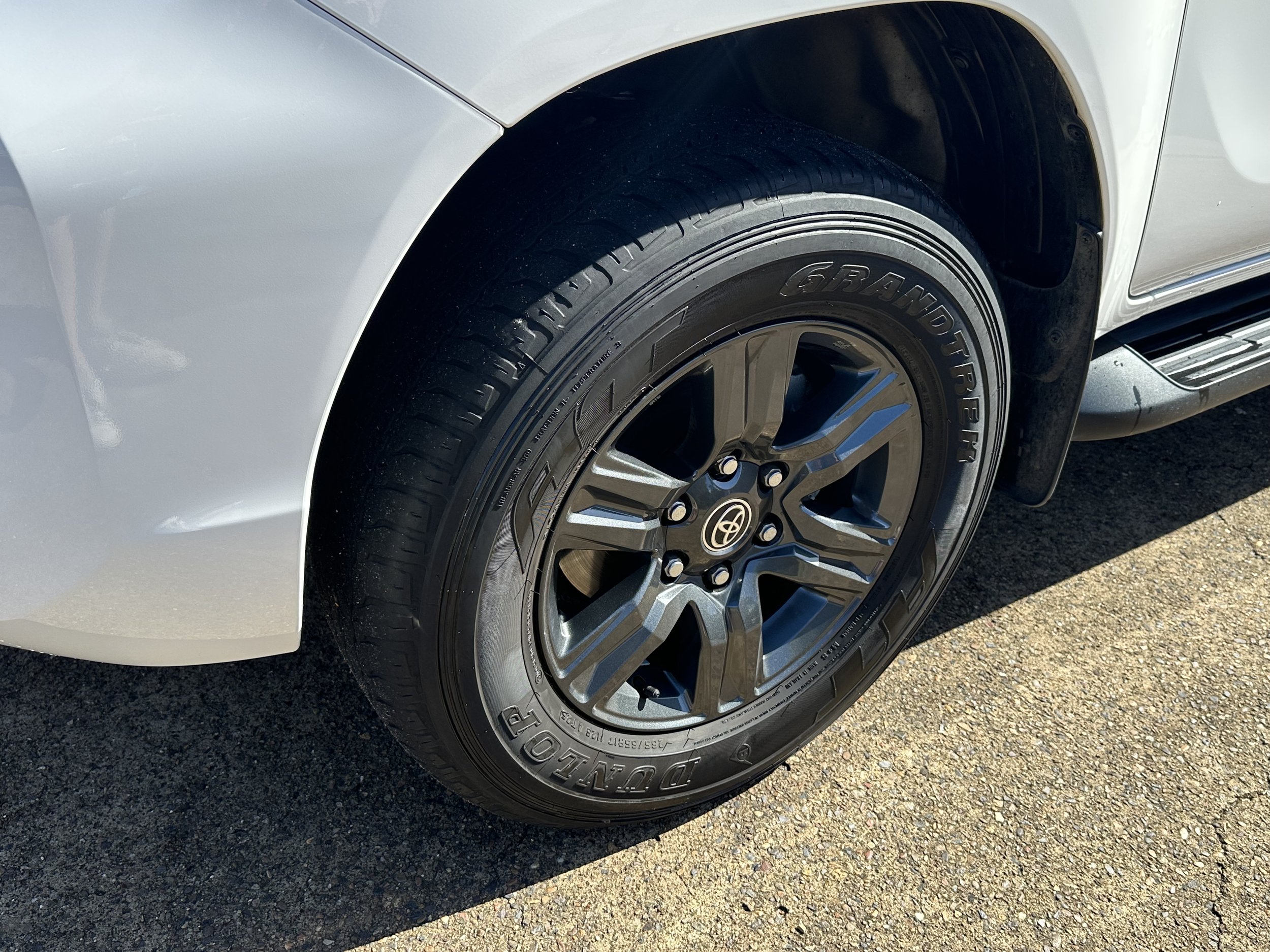 Close-up of a white vehicle's front wheel and tire, with a portion of the silver alloy rim and the vehicle's white body visible.