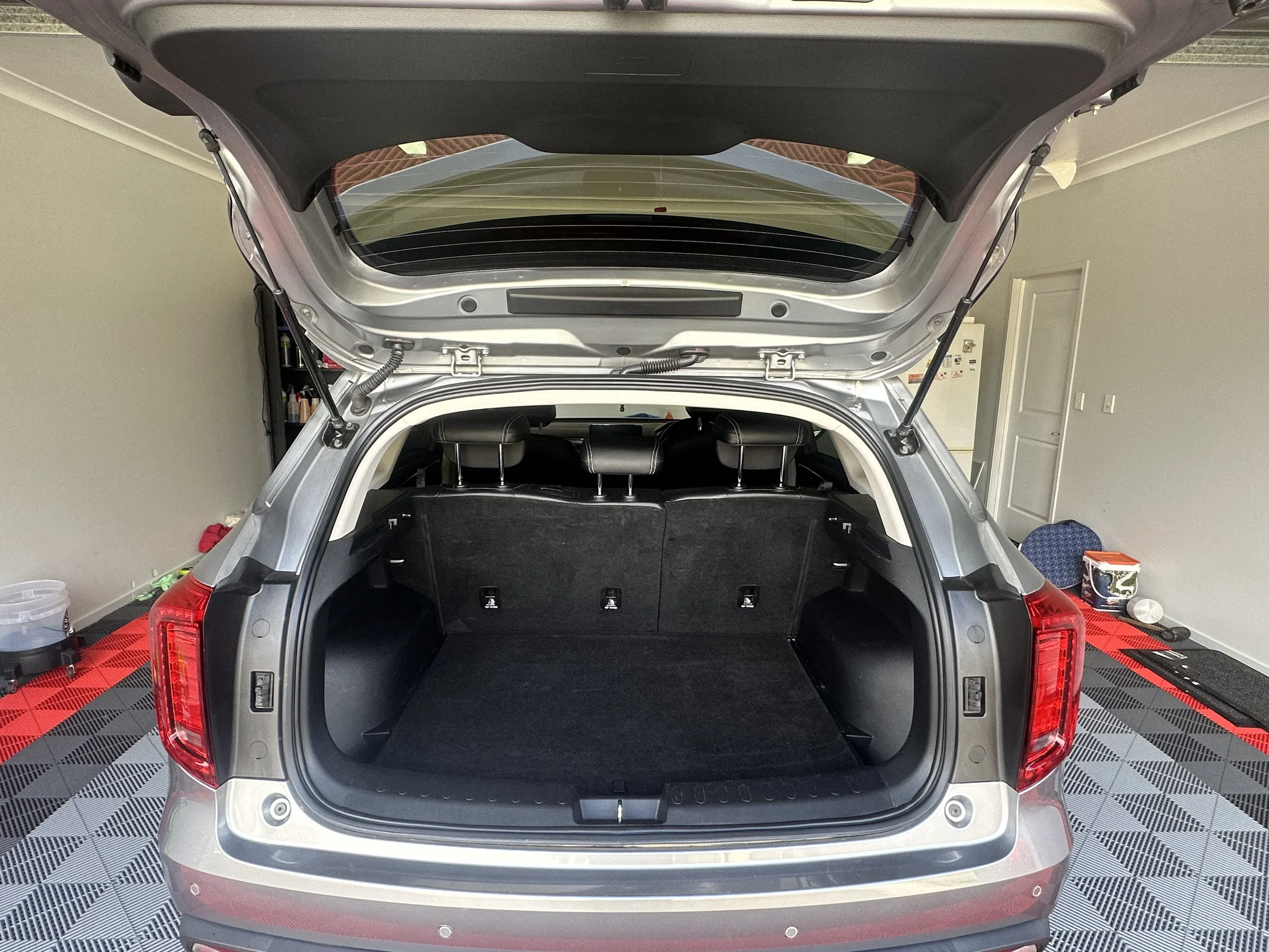 The open trunk of a silver SUV with a black interior, parked indoors on rubber showroom flooring.
