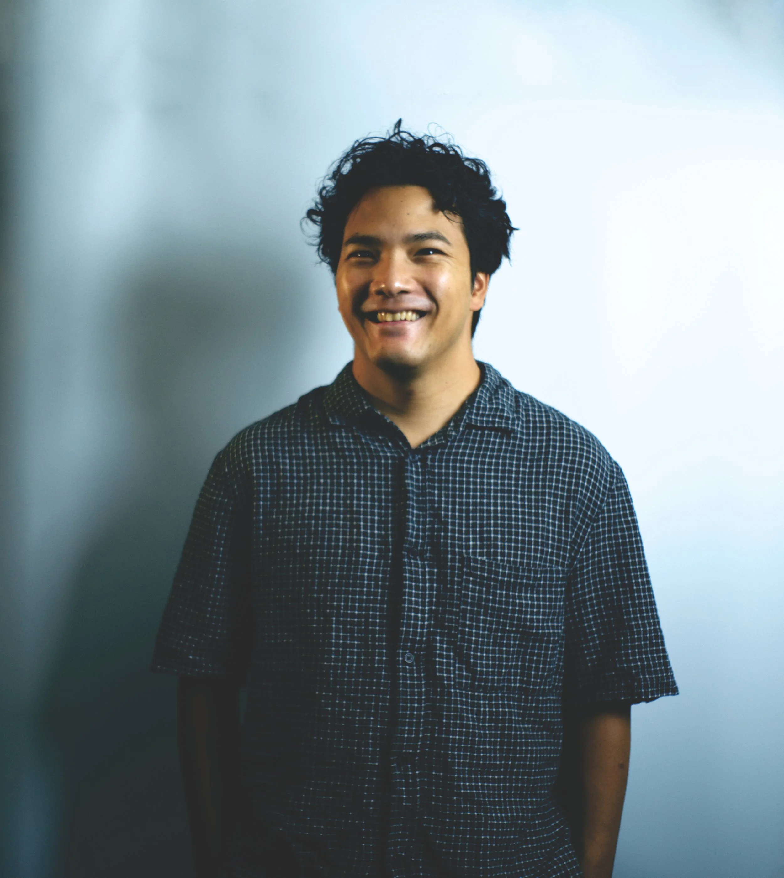 Professional portrait by Sin Stewart, Bangkok videographer, capturing a smiling subject in a clean studio setting with natural lighting.