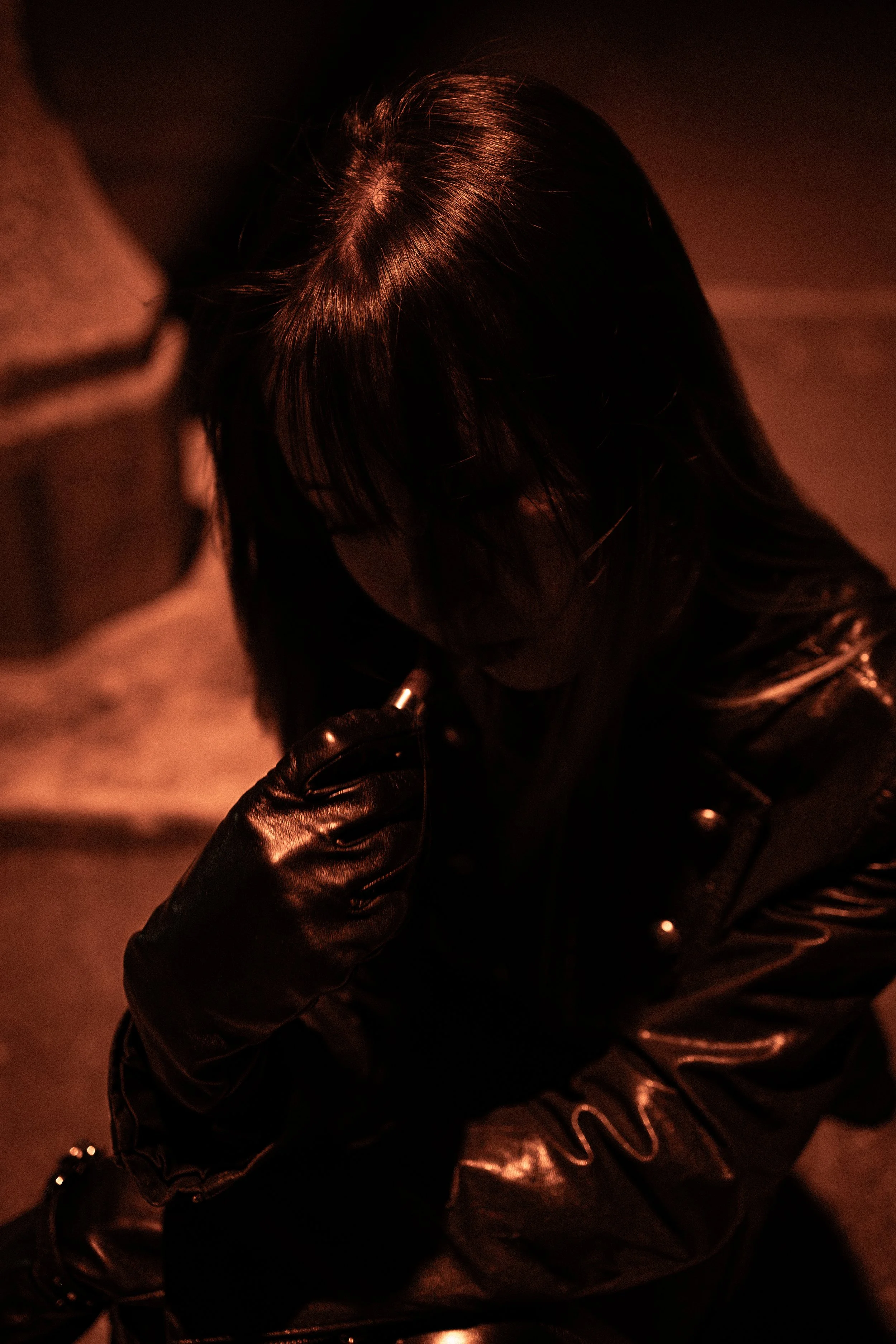 Person with dark hair wearing a leather jacket and gloves, with a dark background, seen from above.