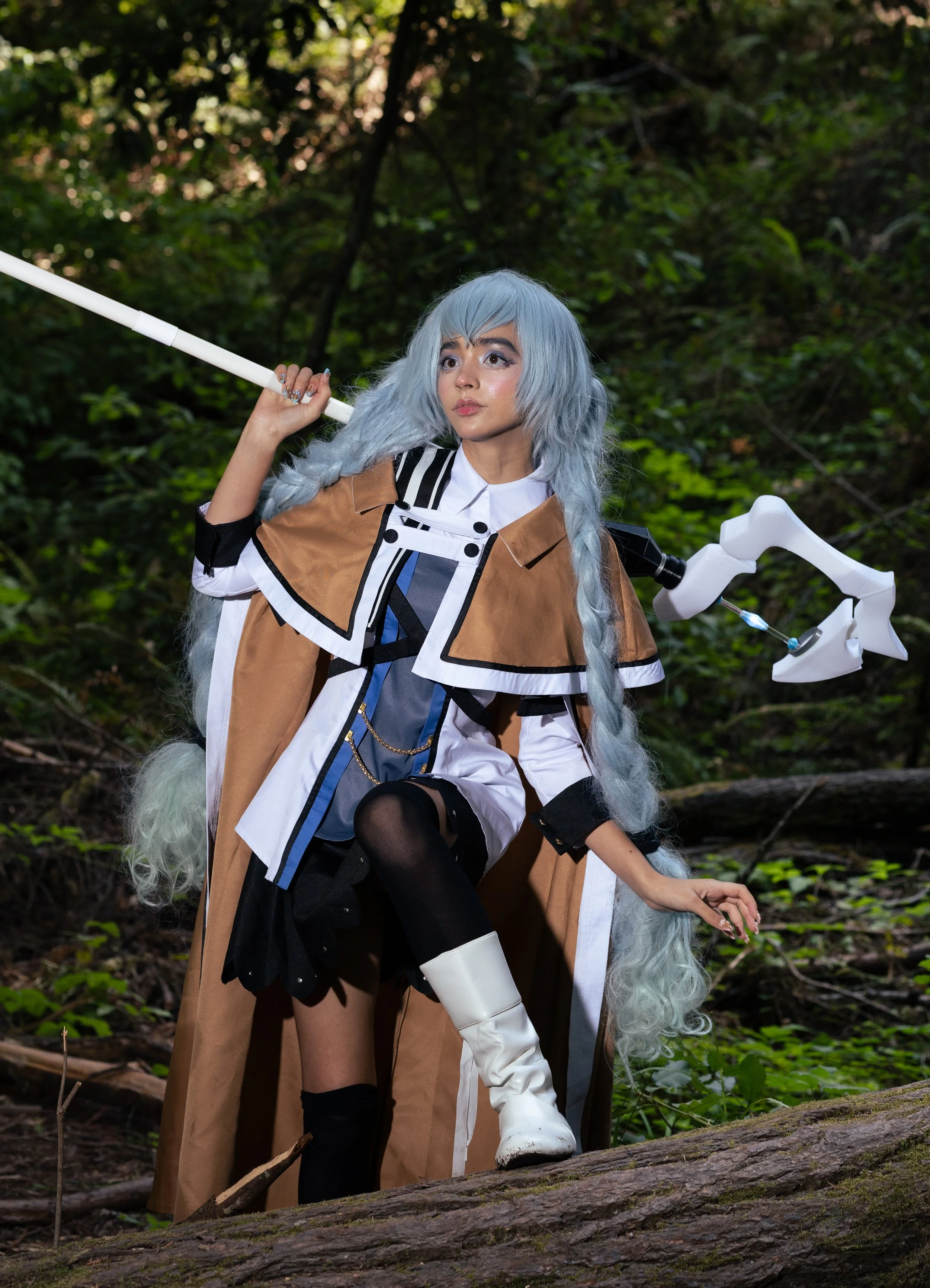 Person dressed as a fantasy character with long blue wig, kimono-style outfit, holding a staff, in a forest setting.