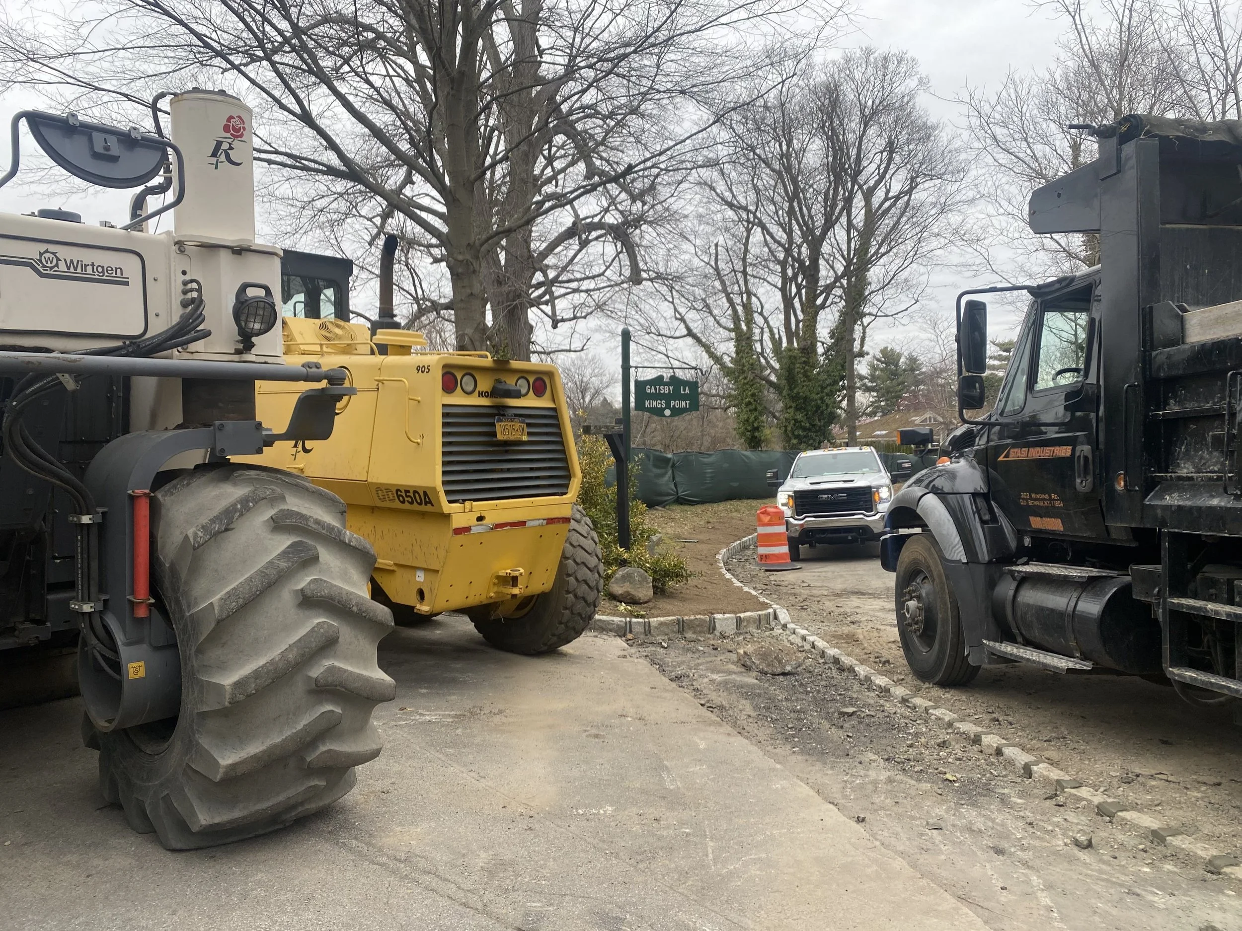 Construction site with yellow excavator and dirt, apartment buildings in the background, traffic light, and street signs.