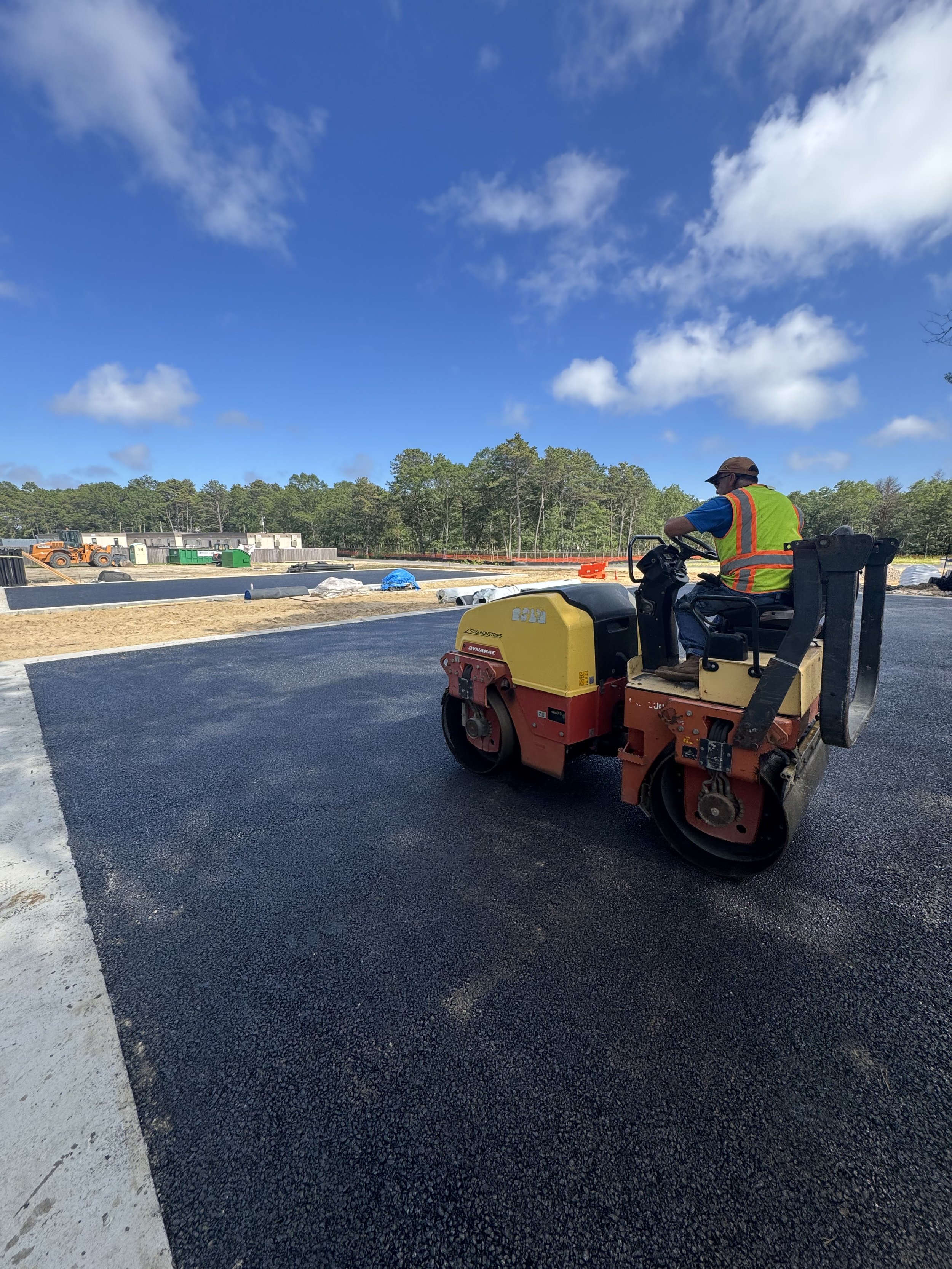 Close-up of large yellow construction roller with orange machinery in the background, on a paved surface.