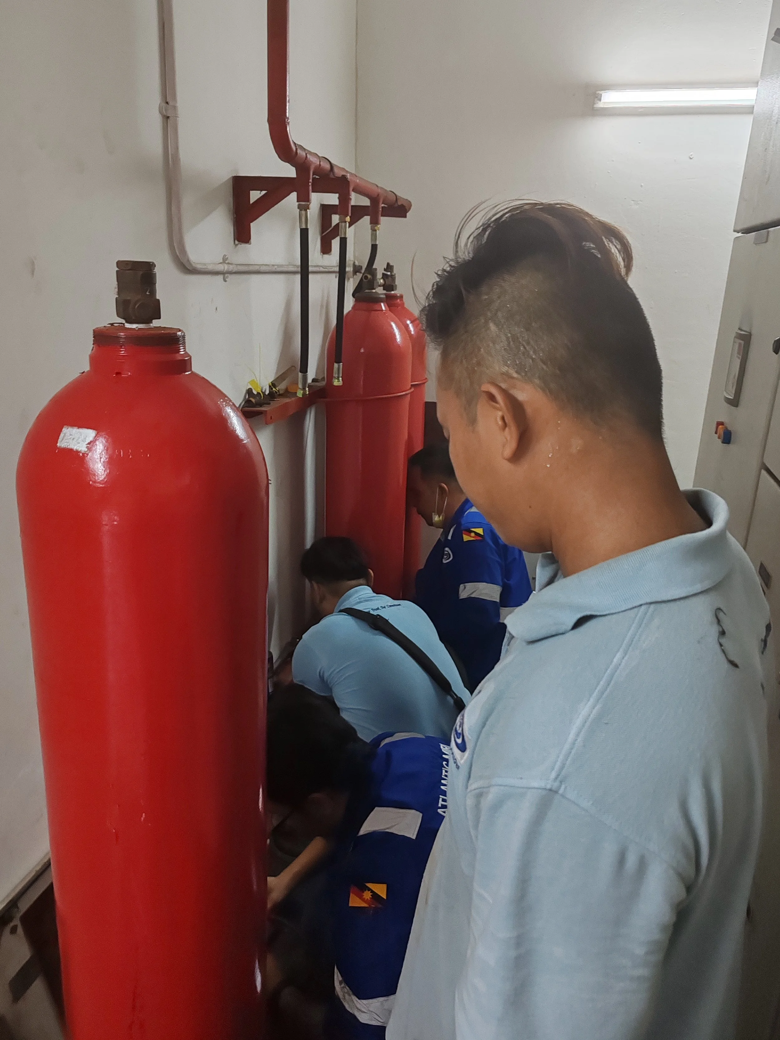 People working on a plumbing system with large red water tanks in a utility room.