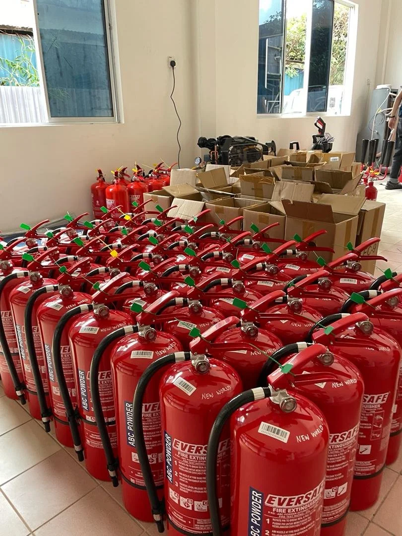 Multiple red fire extinguishers lined up in a room, with some open cardboard boxes and additional extinguishers in the background.