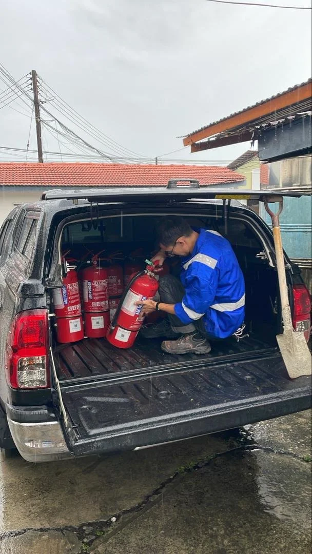 A man in a blue jacket loading fire extinguishers into the back of a pickup truck.