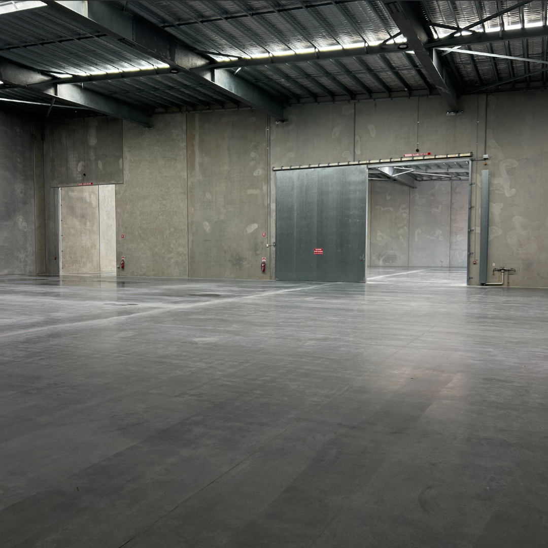 Empty warehouse or industrial space with concrete walls, metal ceiling, and large sliding metal door.