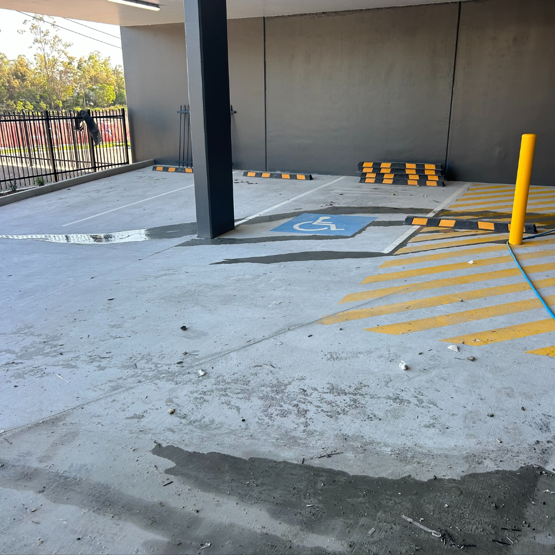 A parking space designated for handicapped individuals with a blue wheelchair symbol painted on the ground, located under a parking structure with some yellow striped area and a yellow bollard.