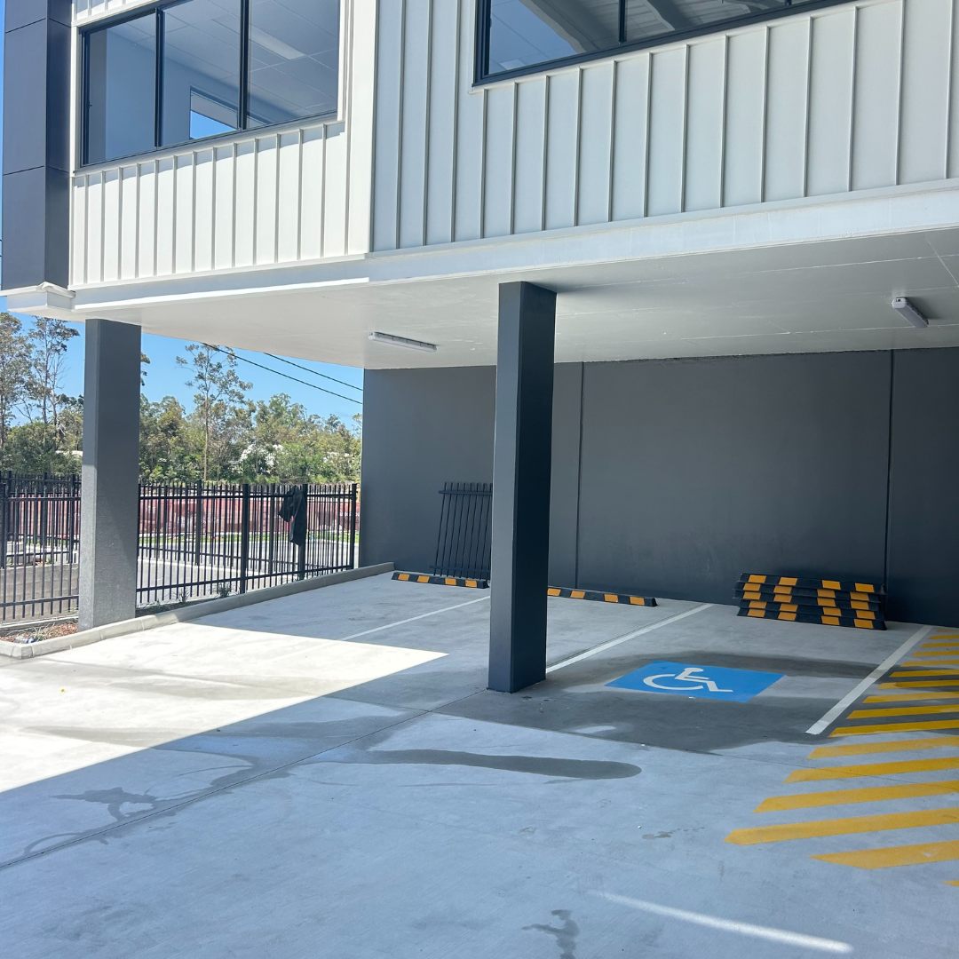 Parking lot with designated accessible parking space marked with wheelchair symbol and yellow striped lines, partially shaded by building overhang.