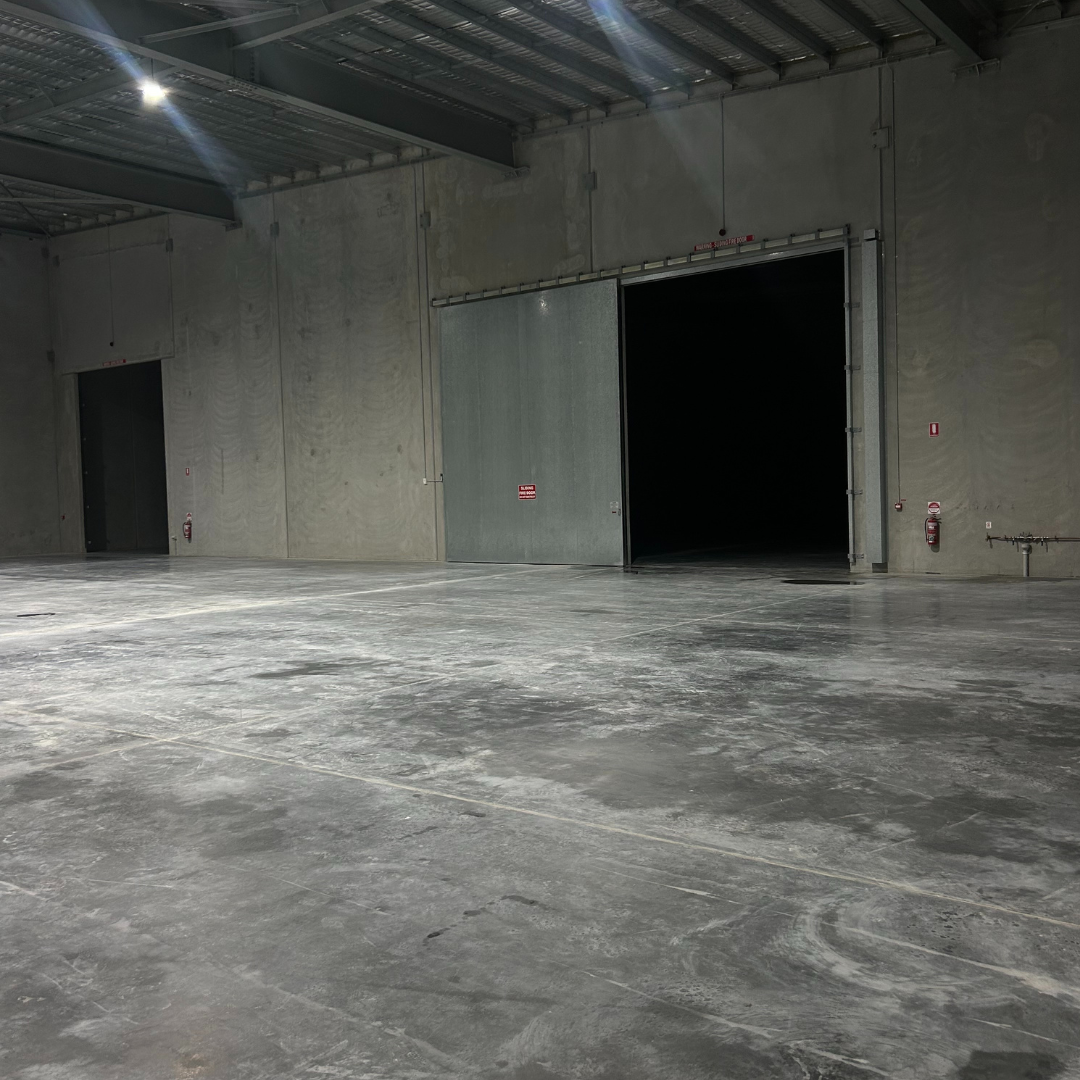 Empty industrial warehouse or storage unit with large open doors, concrete floor, and metal ceiling.
