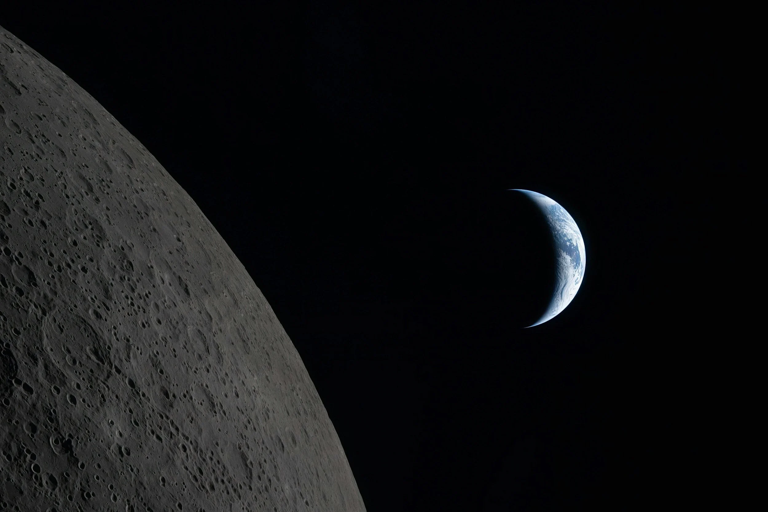 A close-up view of the Moon's cratered surface with Earth visible in the distance against the blackness of space.