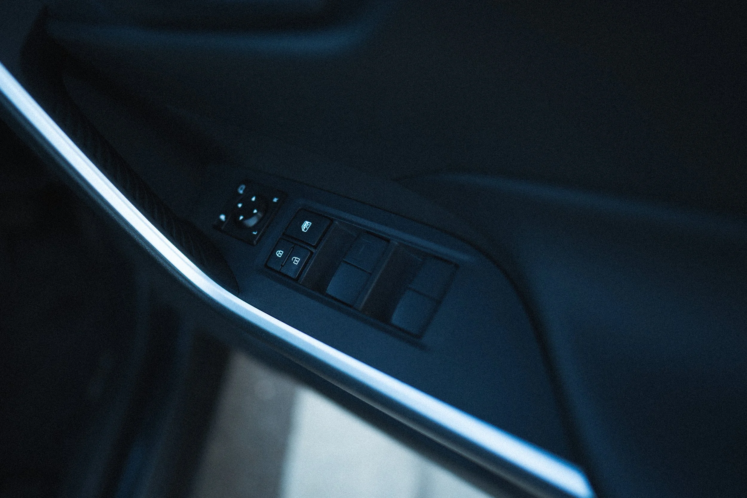Close-up view of the control panel on a car door, showing buttons for window and lock controls, illuminated in low light.