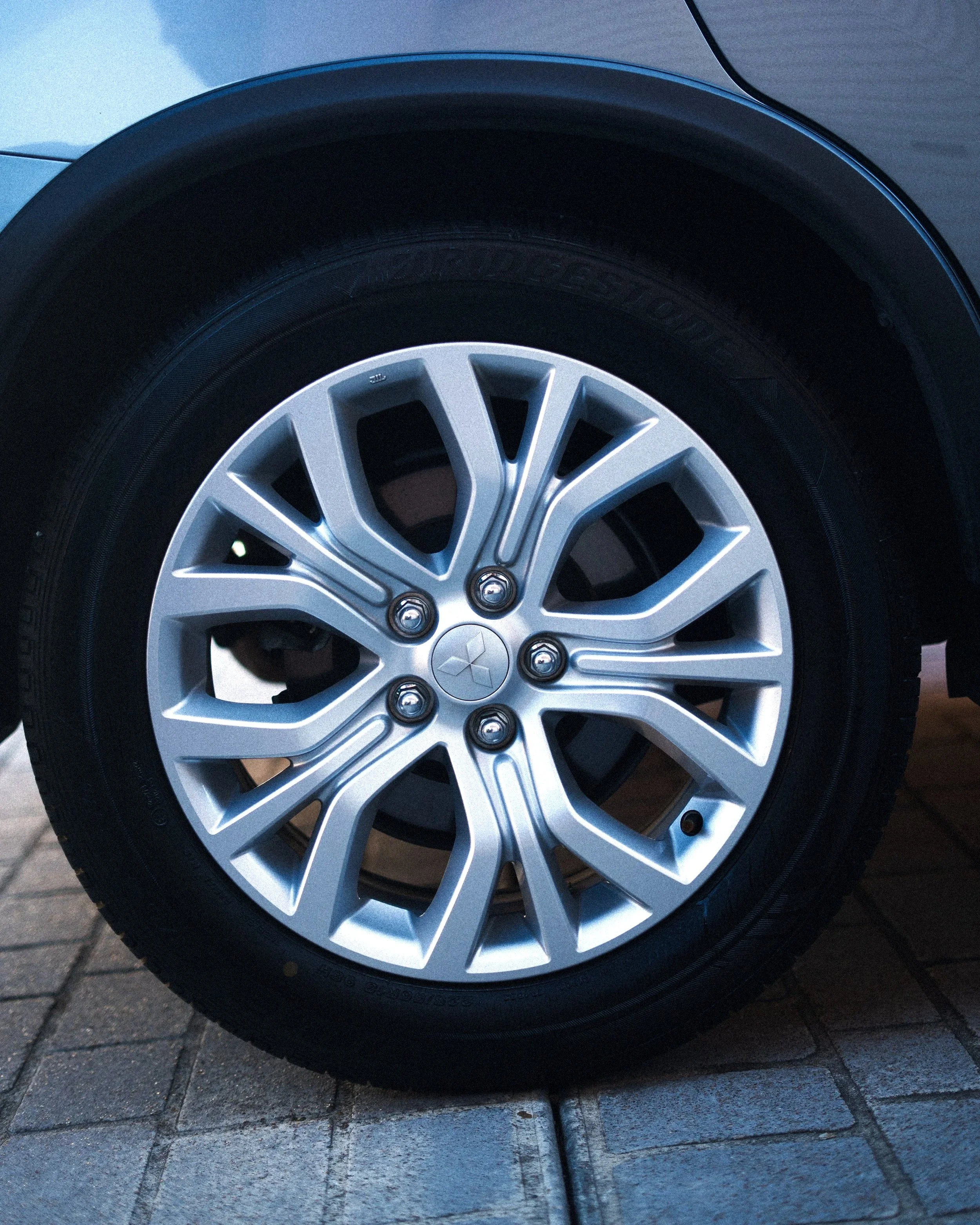 Close-up of a car wheel with a silver alloy rim and black tire, parked on a paved surface.