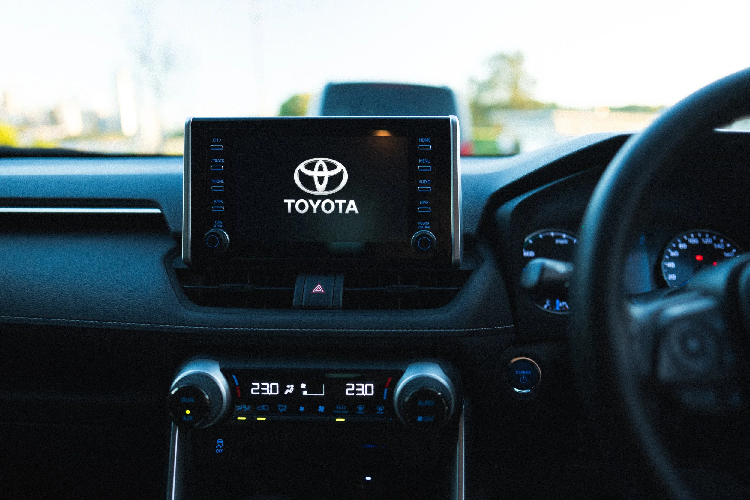 Interior of a car showing the dashboard and infotainment screen with Toyota logo, climate controls, and digital temperature display.