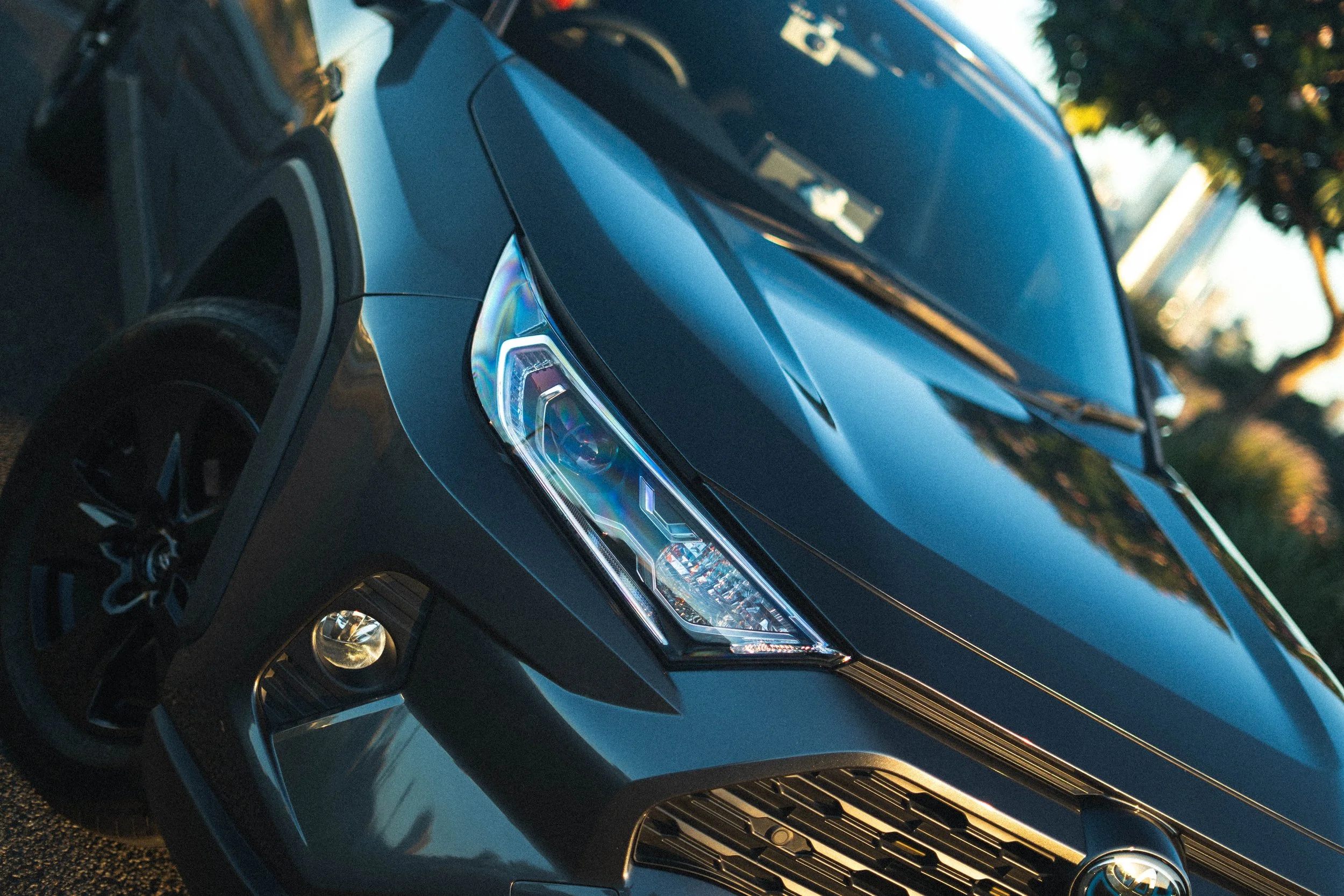 Close-up of a dark blue modern SUV with angular headlights and a prominent front grille, parked outdoors with trees in the background.