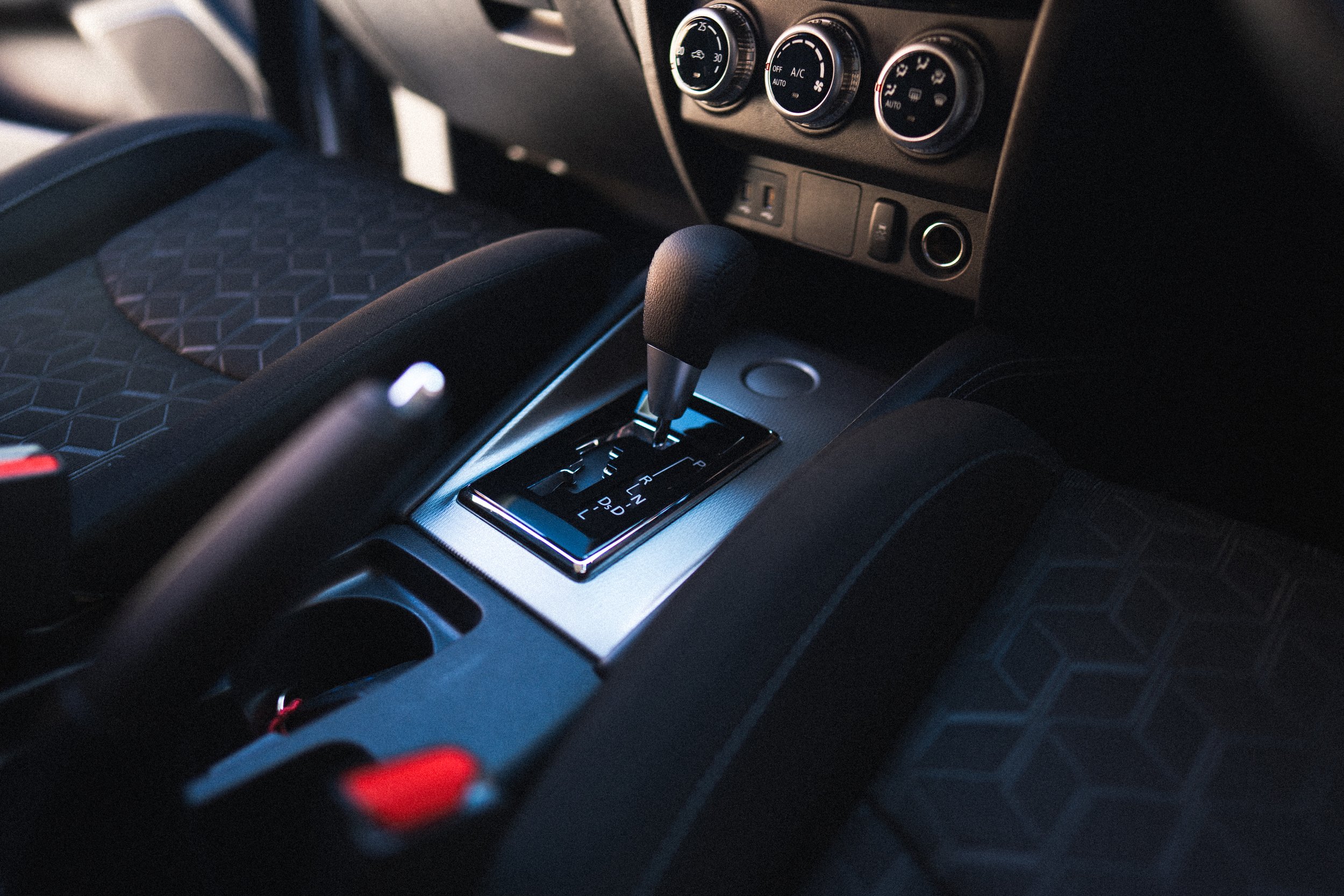 The image shows the interior of a car, focusing on the central console with an automatic gear shift lever and climate control knobs.