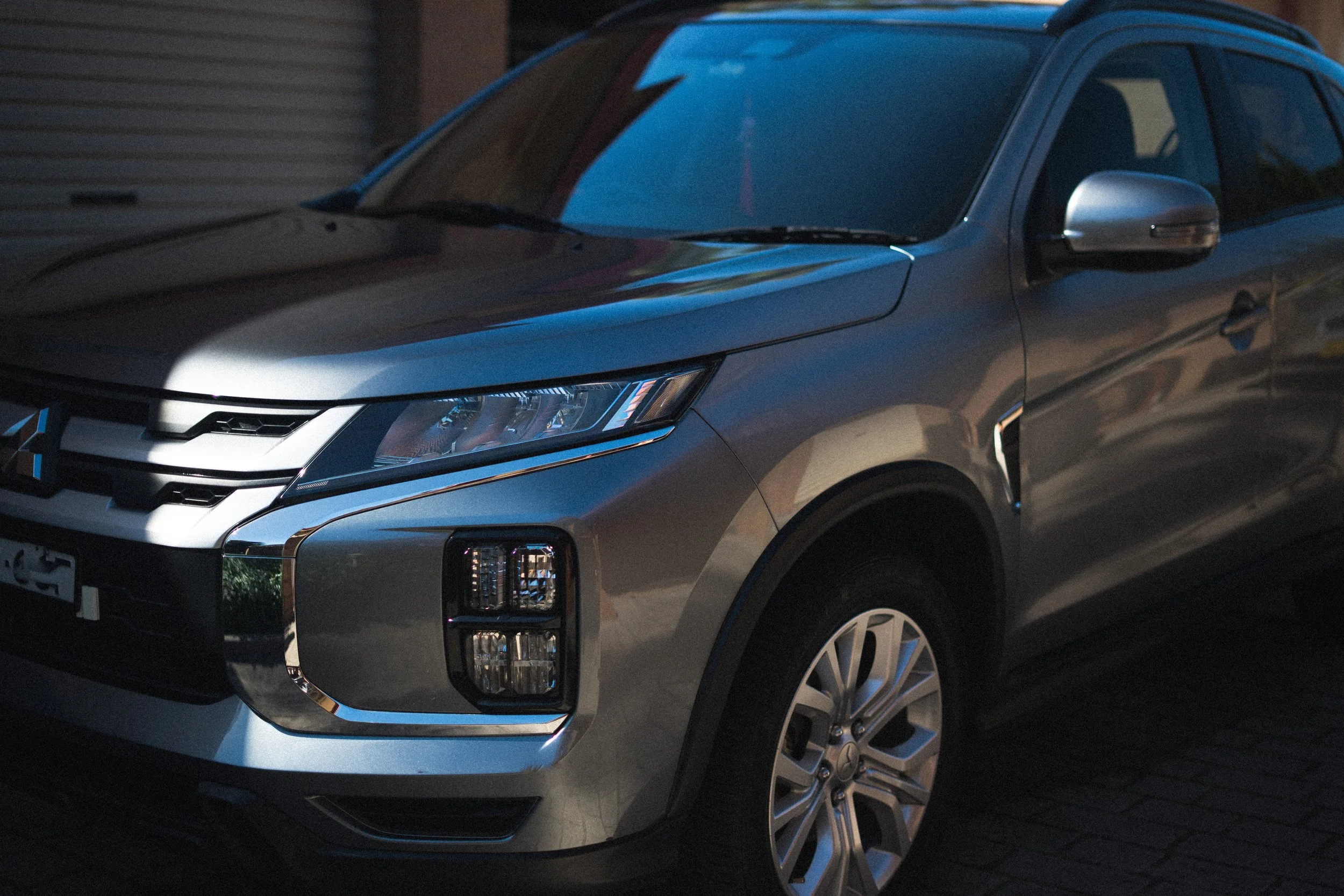 A silver SUV parked outside at dusk, with reflections of the sky on its surface and a partially visible garage door in the background.