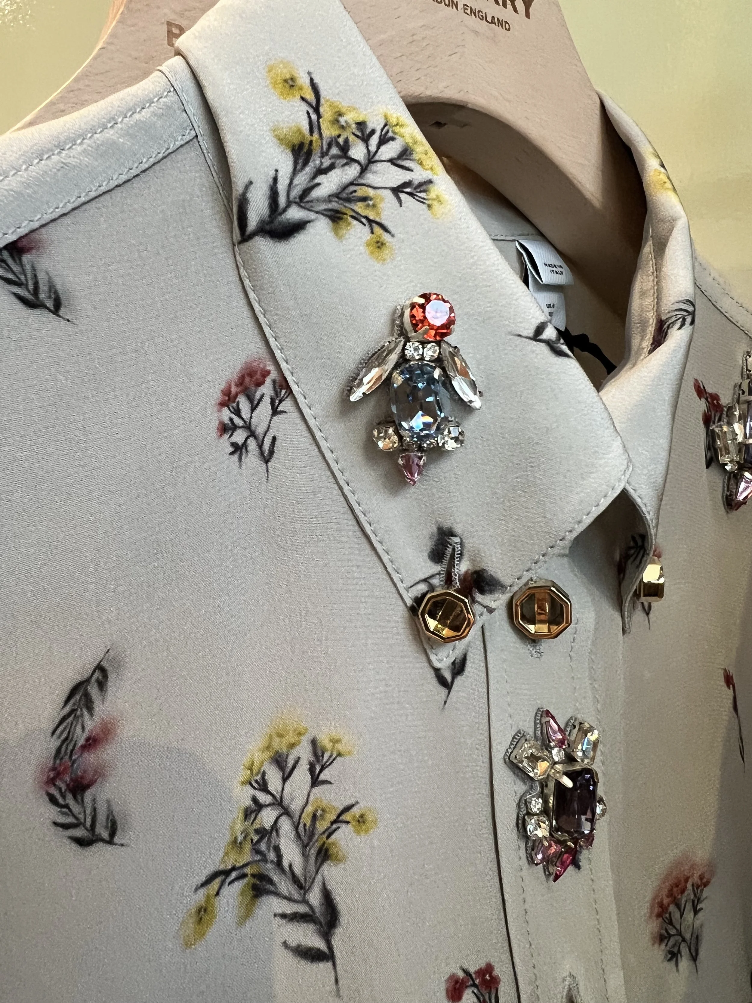 Close-up of a floral print fabric with black, yellow, red, and pink flowers and leaves, adorned with a decorative spider-shaped brooch embellished with various gemstones.