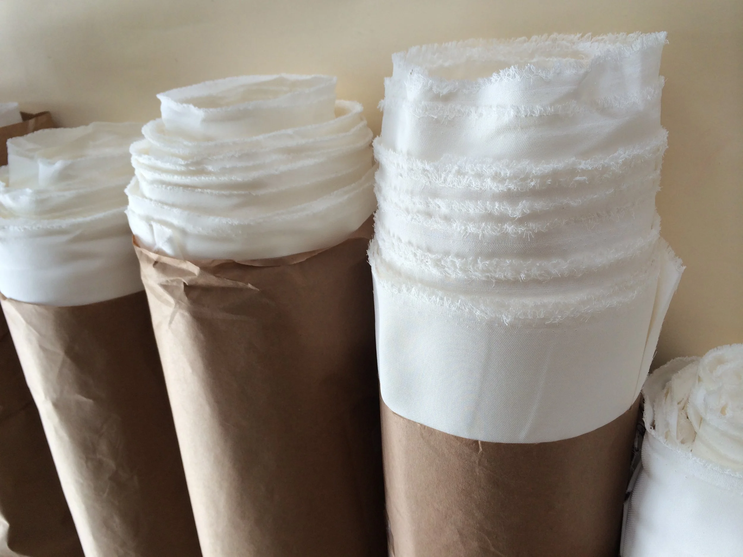 Stacked white fabric strips with frayed edges and satin ribbons, arranged in neat columns.