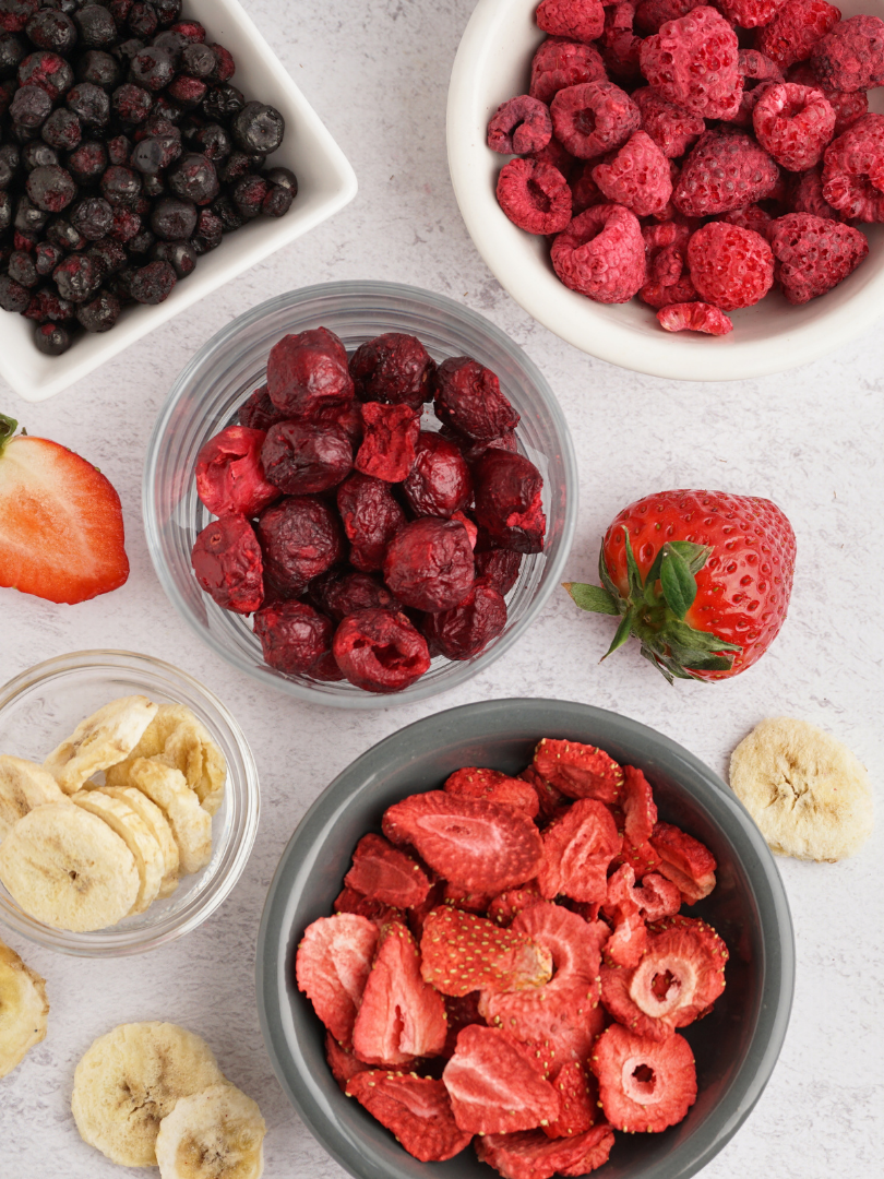 Various types of frozen berries, including blueberries, raspberries, strawberries, and sliced banana on a light background.