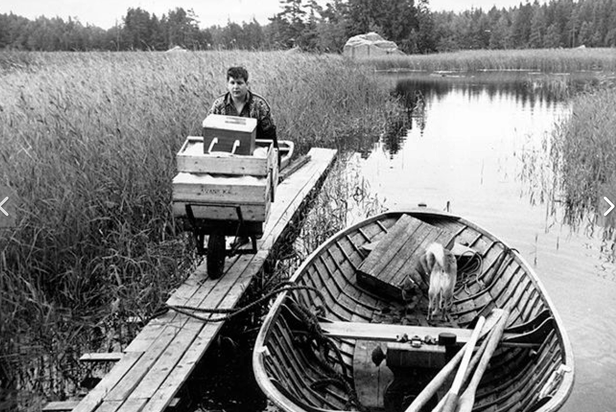 Mies vanhanaikaisessa mustavalkokuvassa, kalalaatikot ja soutuvene Pyhtään saaristossa.