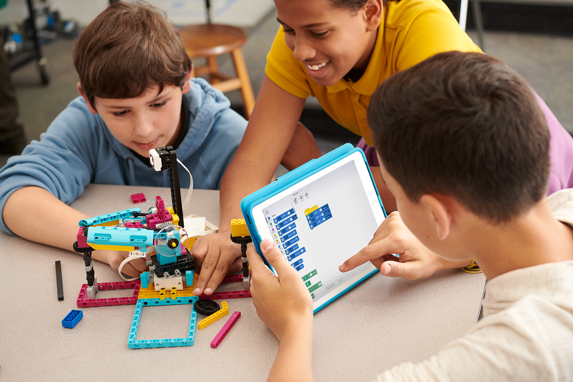 Drie kinderen werken samen aan een robot gebouwd met LEGO, terwijl ze een tablet gebruiken om de programmeercode te bekijken en te bewerken.