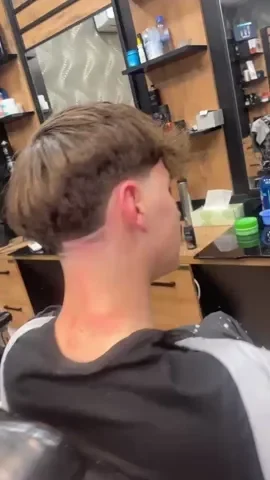 Side view of a young man with light brown hair getting a haircut in a barber shop.