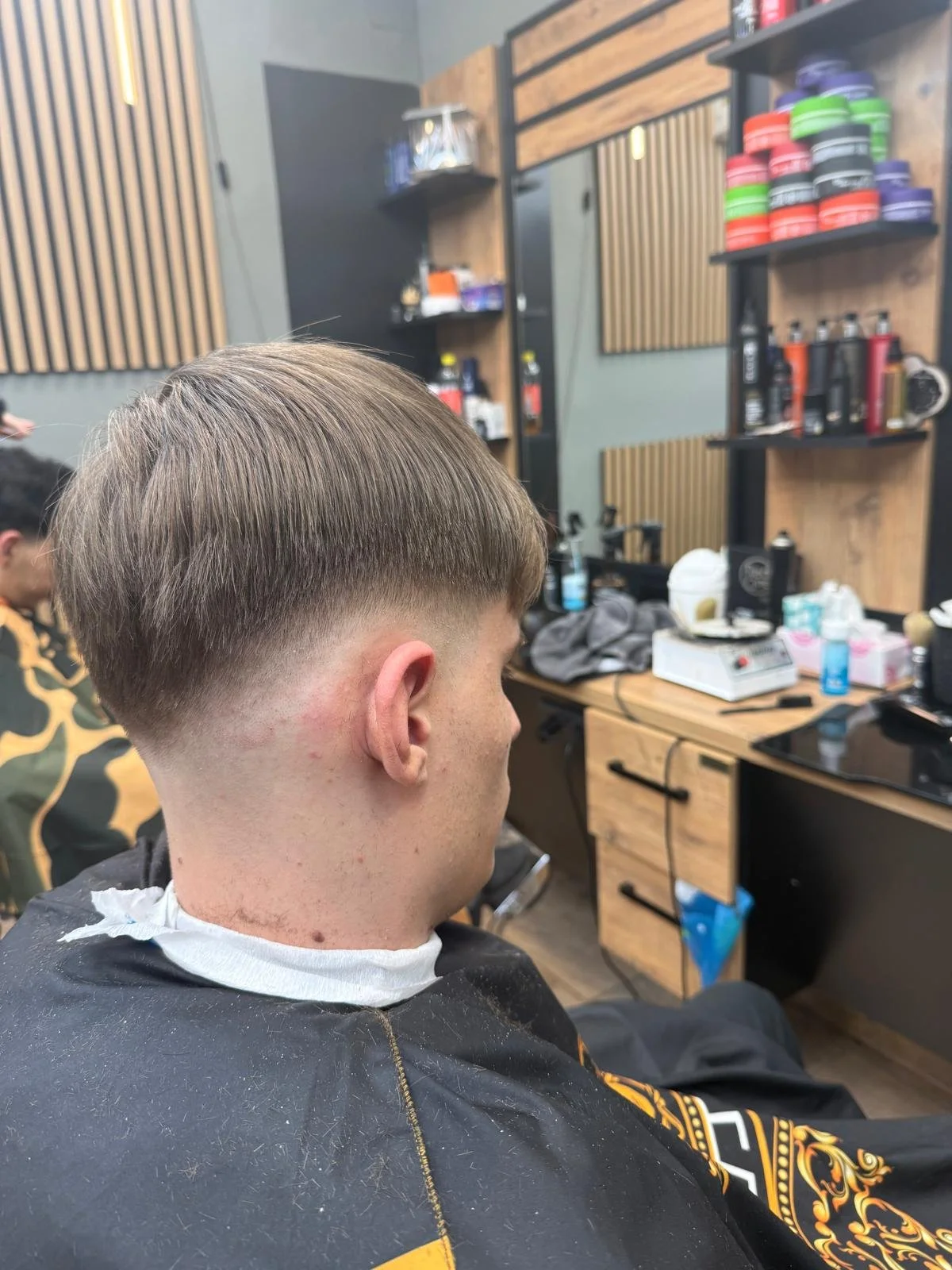 A young man with a fresh fade haircut sitting in a barber shop.