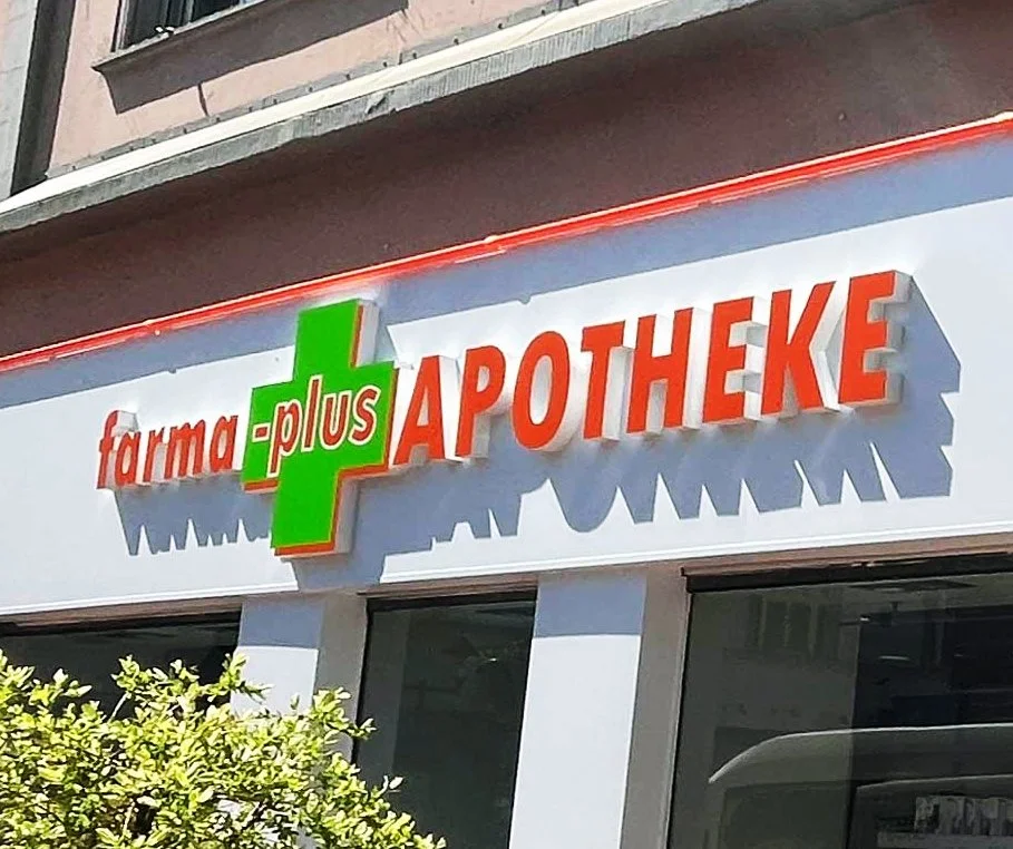 Außenansicht eines Arzneimittelgeschäfts mit einem Schild, das 'Farmaplus Apotheke' heißt.