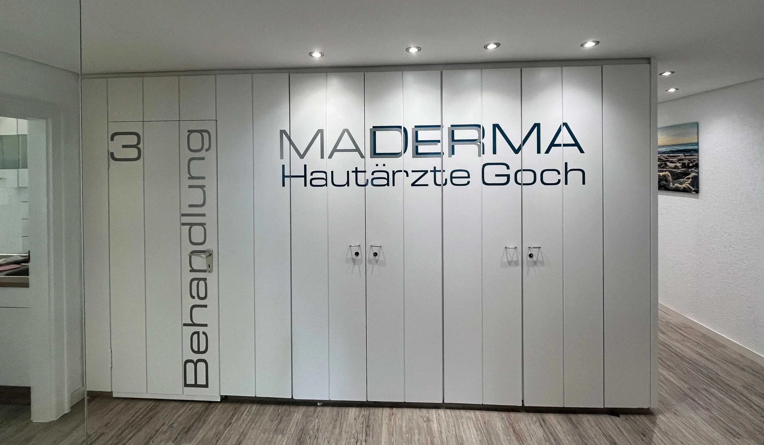 Weiße Wand mit schwarzen Buchstaben, die auf verschiedene Begriffe im Zusammenhang mit Hautgesundheit und dermatologischer Praxis hinweisen, inklusive 'MADerma' und 'Hautärzte Goch'.