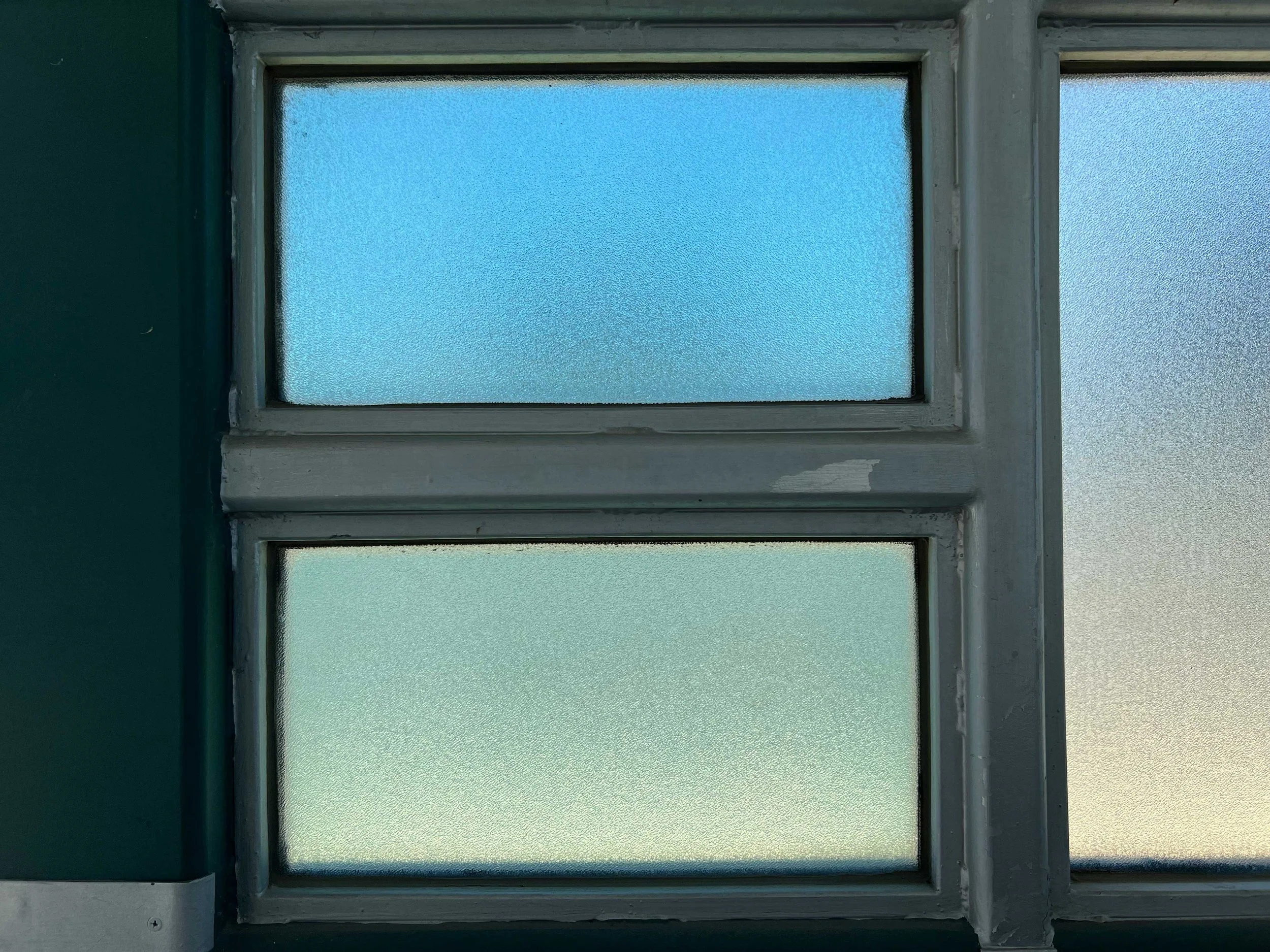 Drei Fenster mit Milchglas in einem Haus, die Fensterrahmen sind weiß, die Wand ist grün.