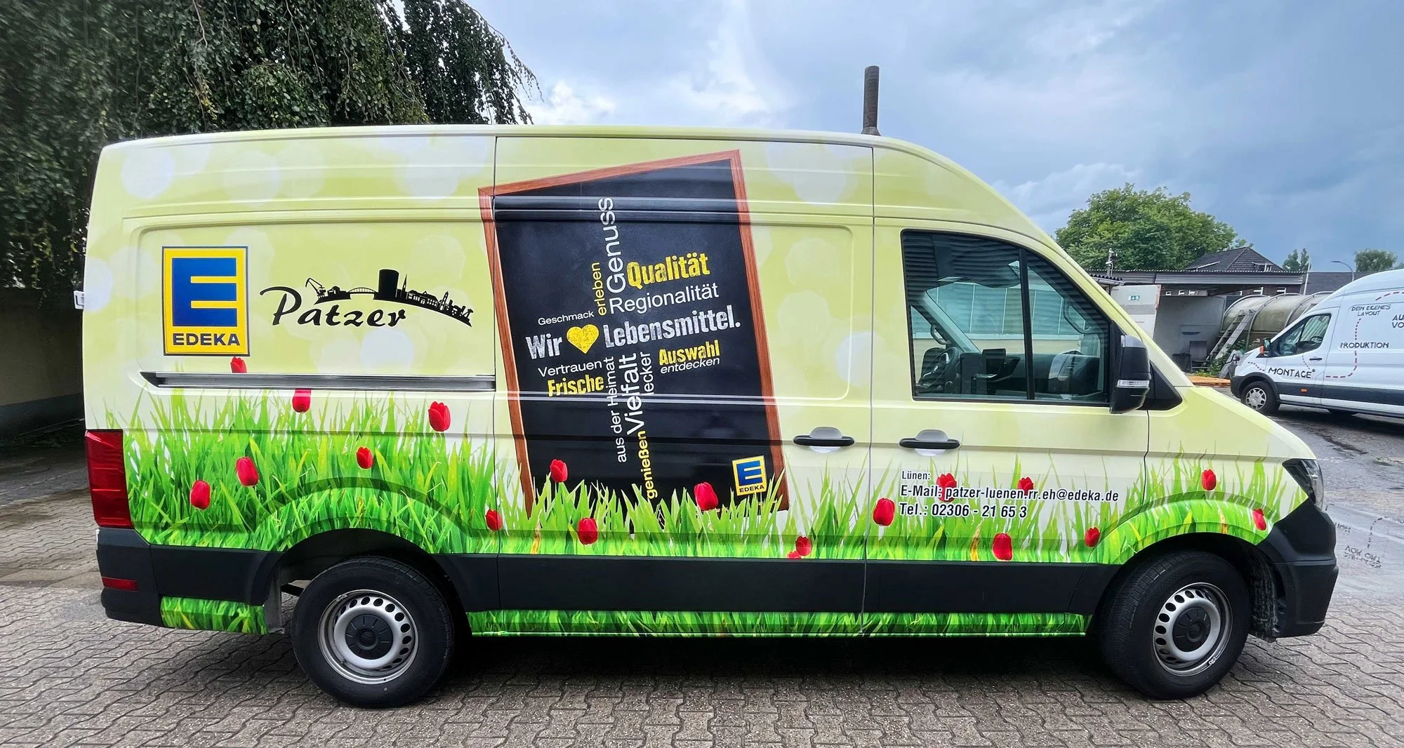 Werbevehikel mit Edeka-Logo, Gras- und Tulpenmuster, Werbung für regionale Lebensmittel, Kontaktinformationen auf der Seite.