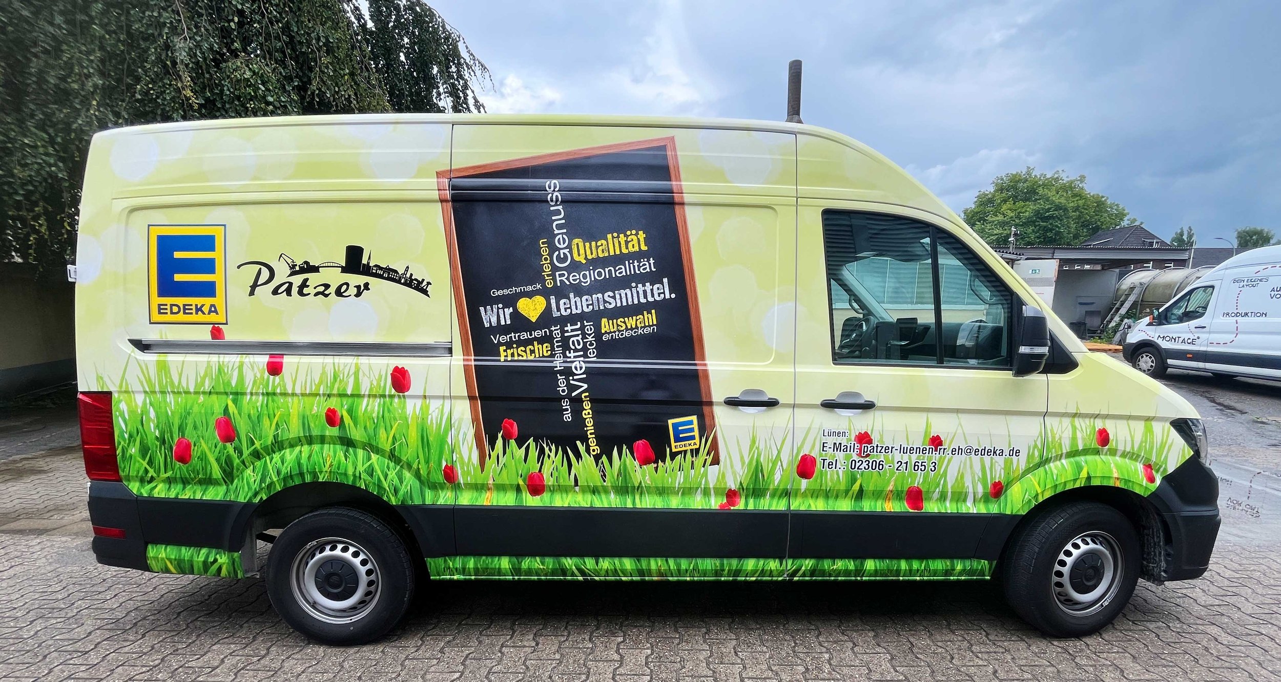 LKW-Transporter mit Werbung von EDEKA Patzer, grüne Wiese mit roter Tulpe Muster, Werbung für Lebensmittel mit Fokus auf Qualität, Regionalität und Frische, Kontaktinformationen inklusive E-Mail und Telefonnummer auf der Seite.