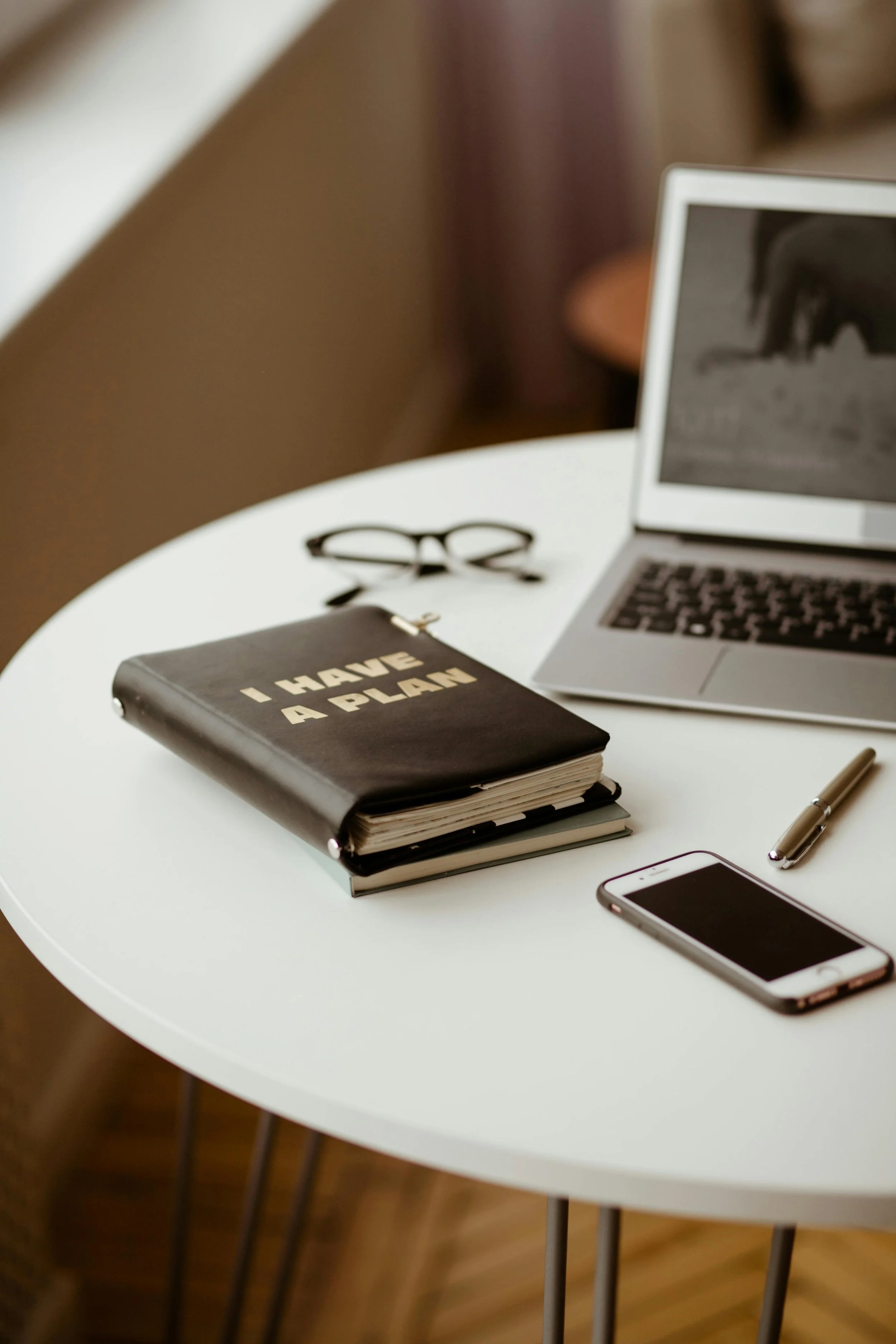 Desk with laptop glasses cell phone and leather planner titled I Have a Plan representing content strategy