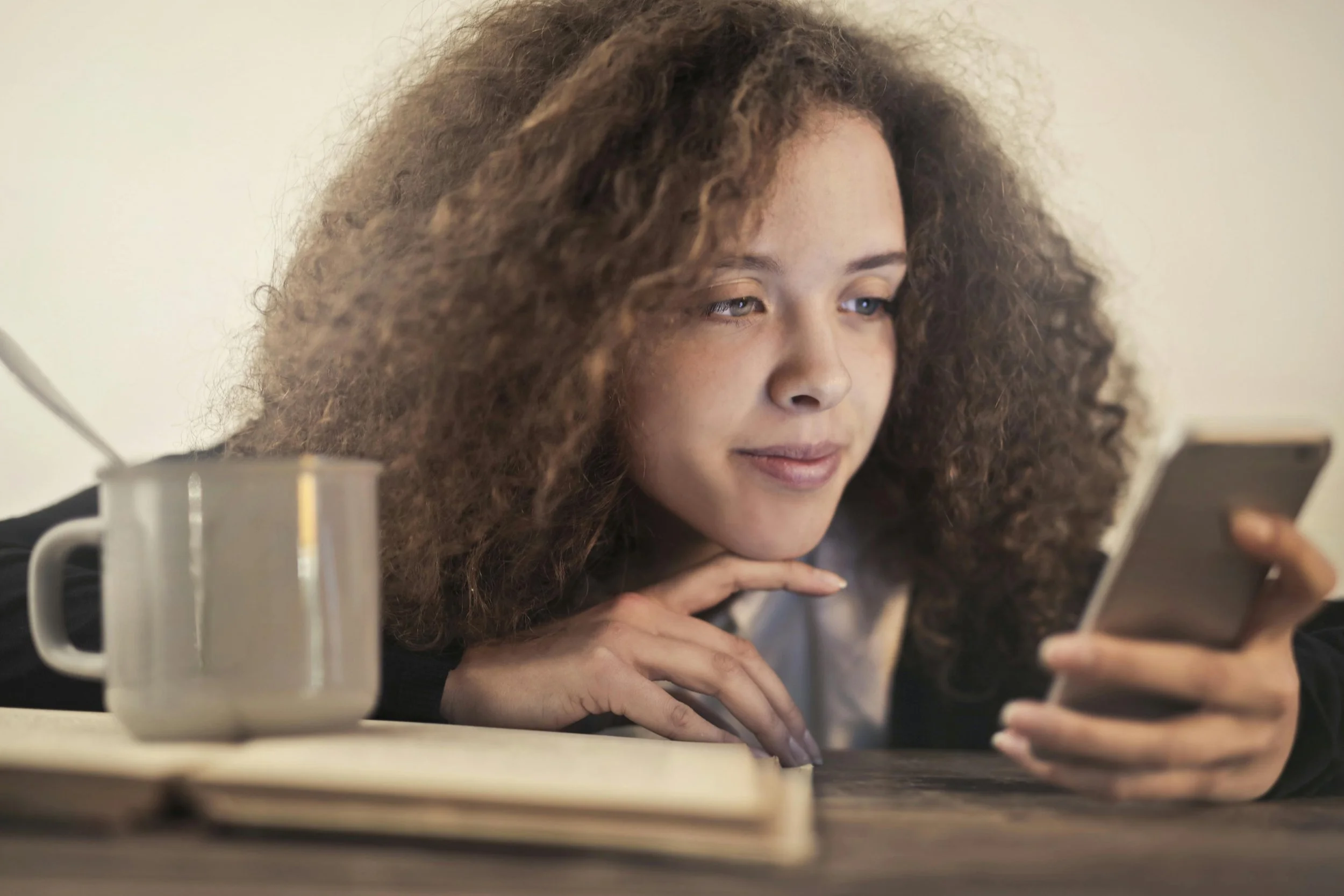 Young woman reading health information on her phone while sitting at a table with coffee and an open book