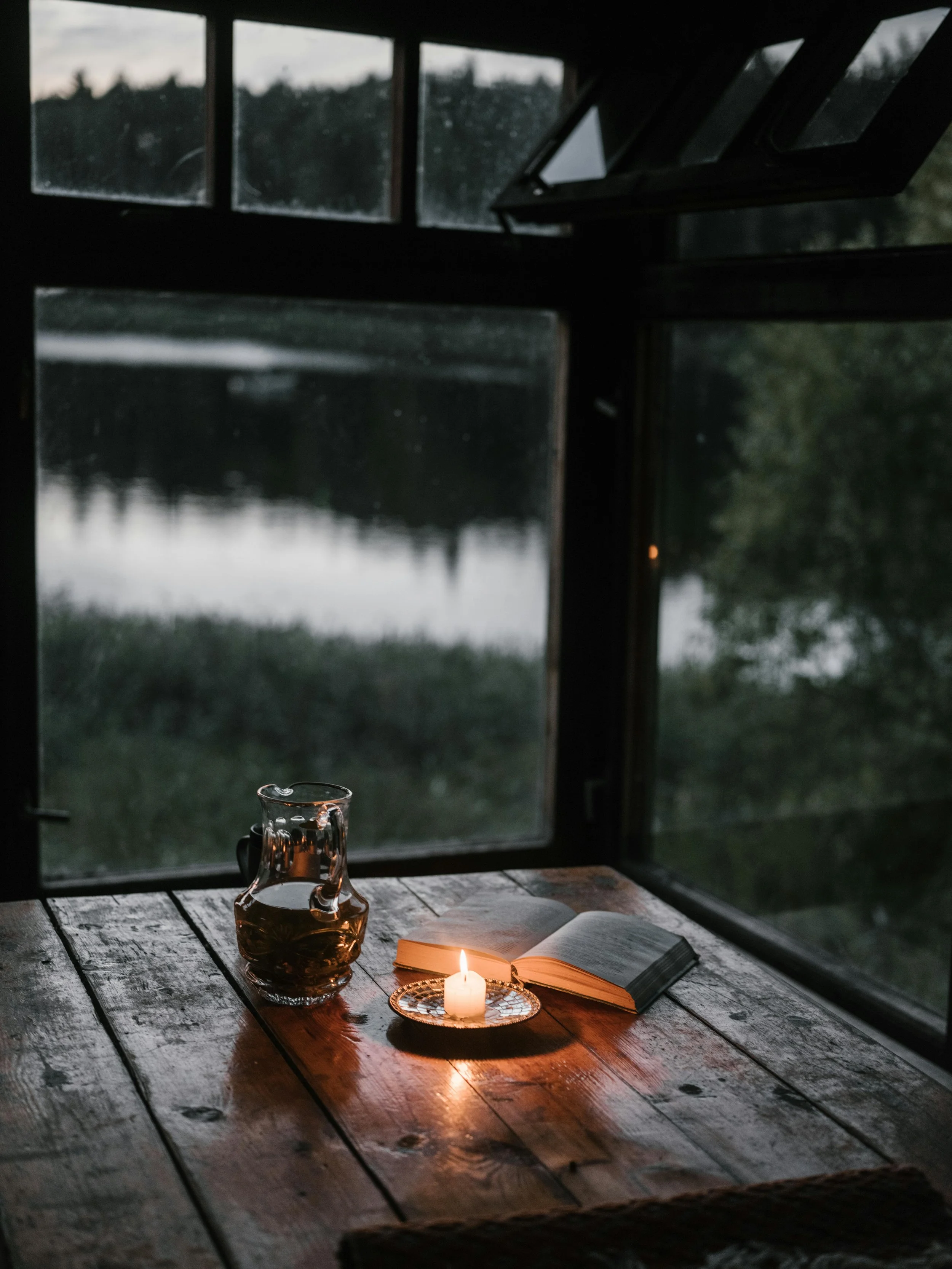 Candlelit scene with open book on wooden table beside a window overlooking a lake representing thoughtful reflection in healthcare communication