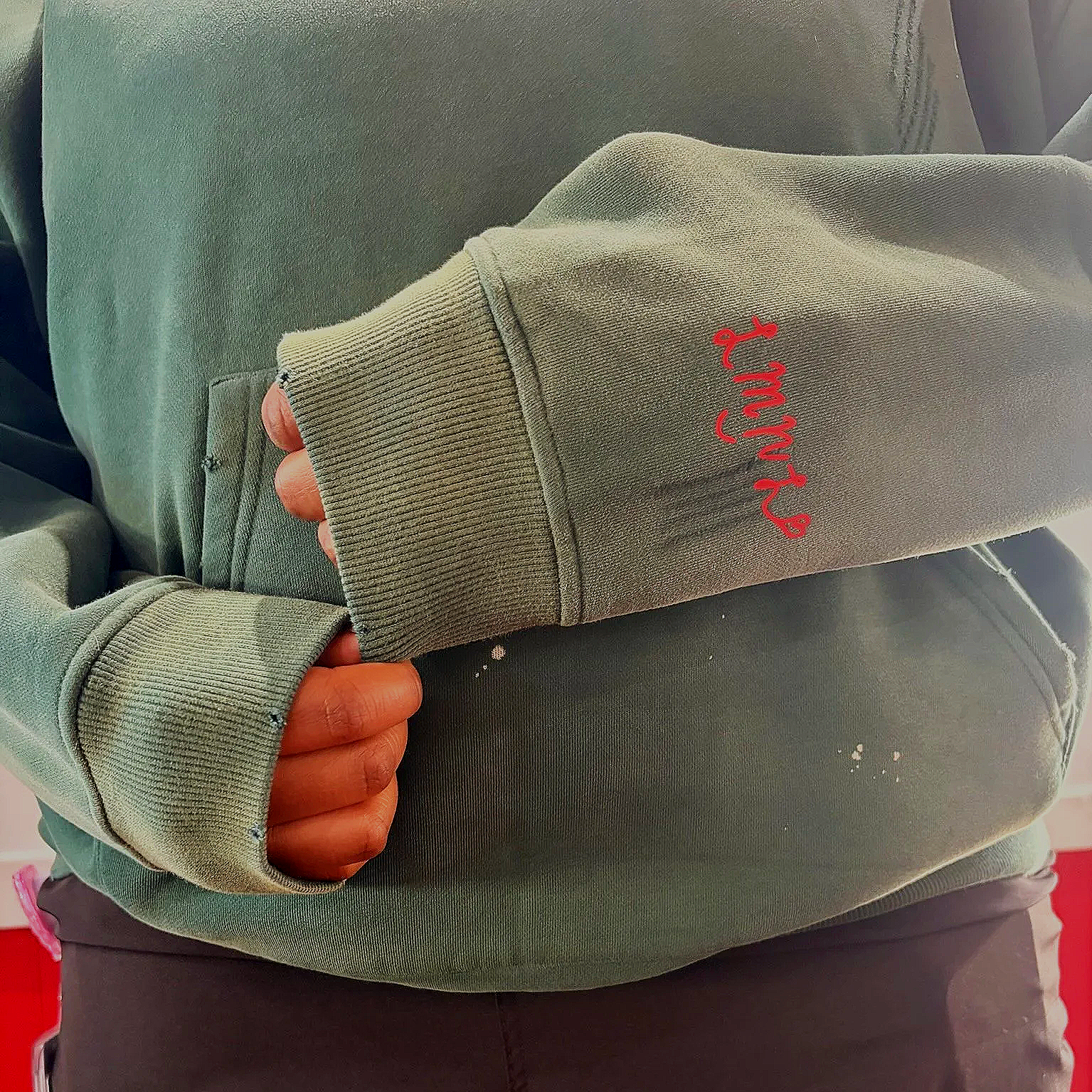 Close-up of a person wearing a green hoodie with the words 'art night' embroidered in red on the sleeve, taking a selfie in a mirror. The person's hand is partially visible, and the hoodie has a ribbed cuff.